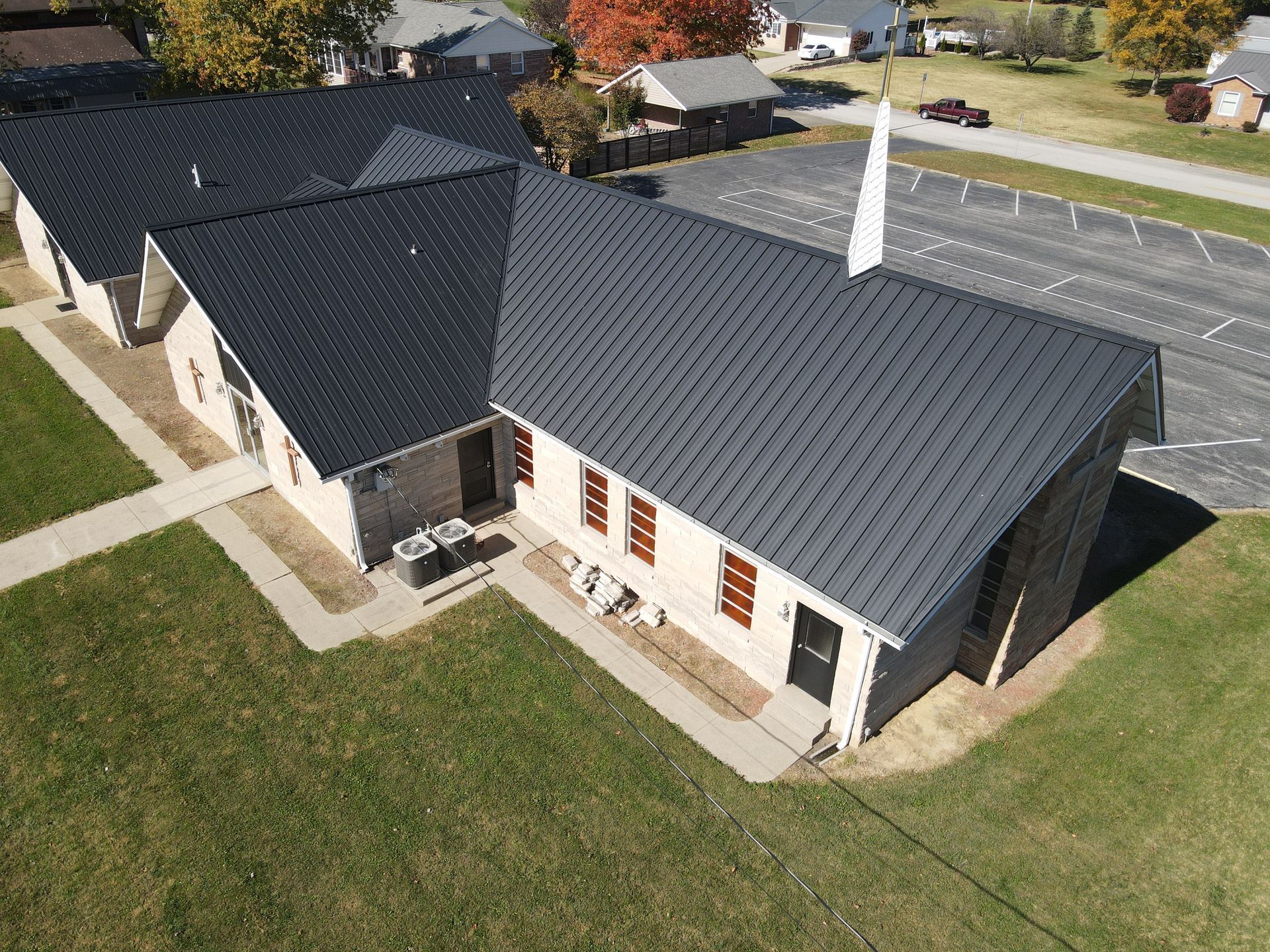 Aerial view of a single-story house with a dark roof, white exterior, and surrounding lawn.