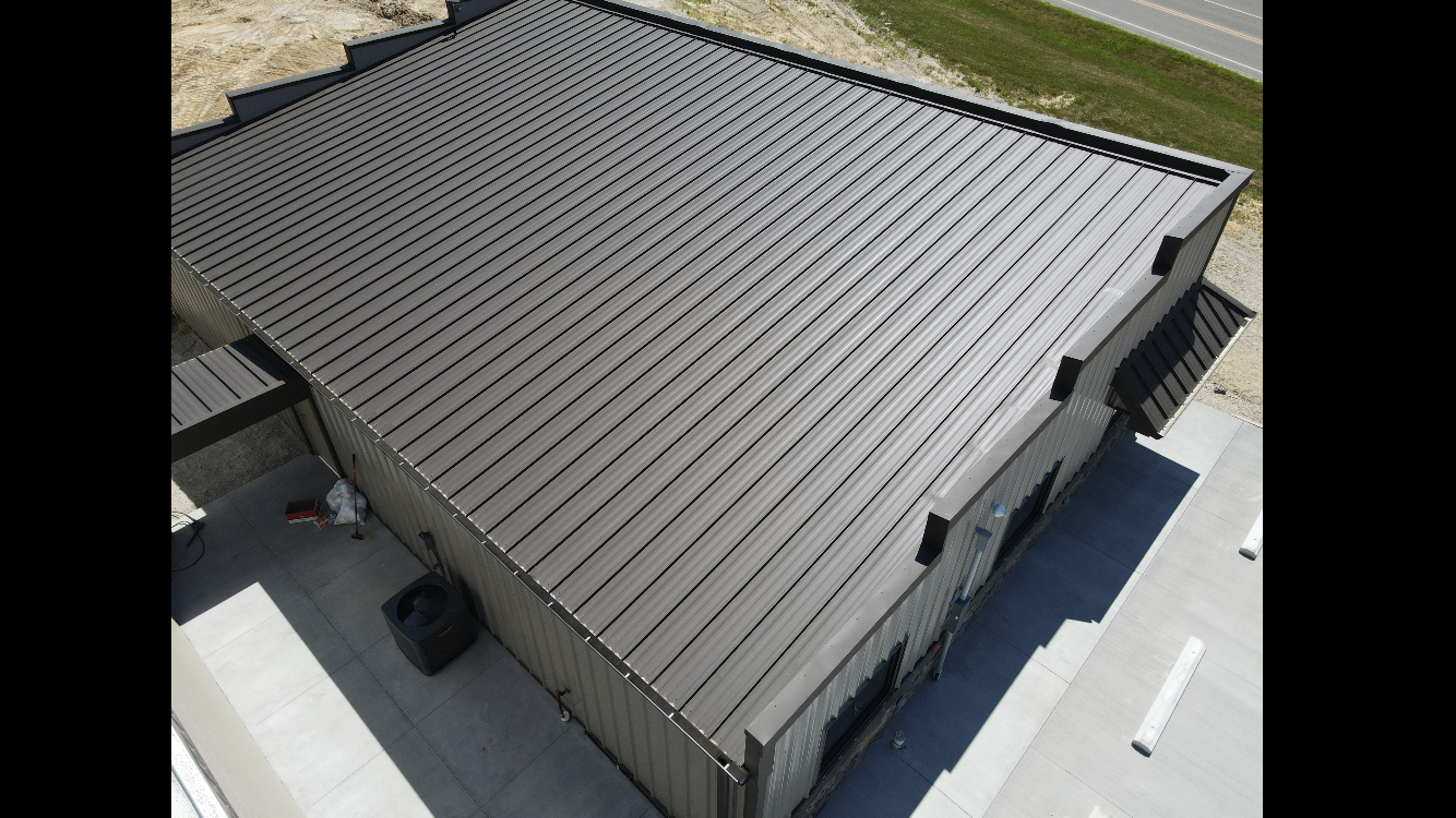 Aerial view of a gray ribbed metal roof on a building with white trim and surrounding pavement.