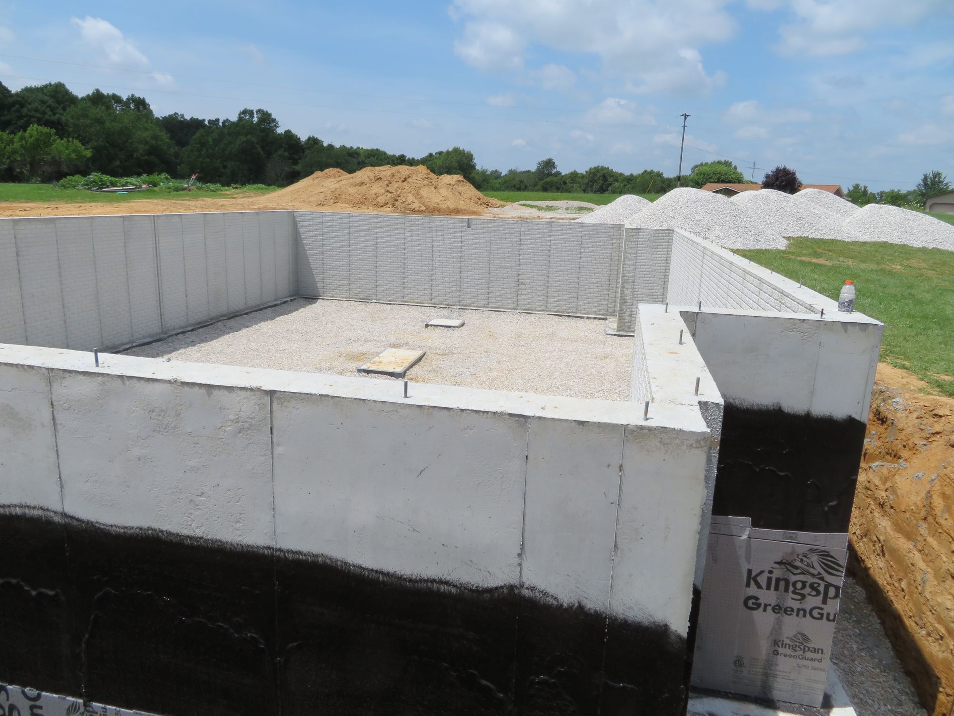 Concrete foundation walls under construction with gravel floor and dirt piles in the background.