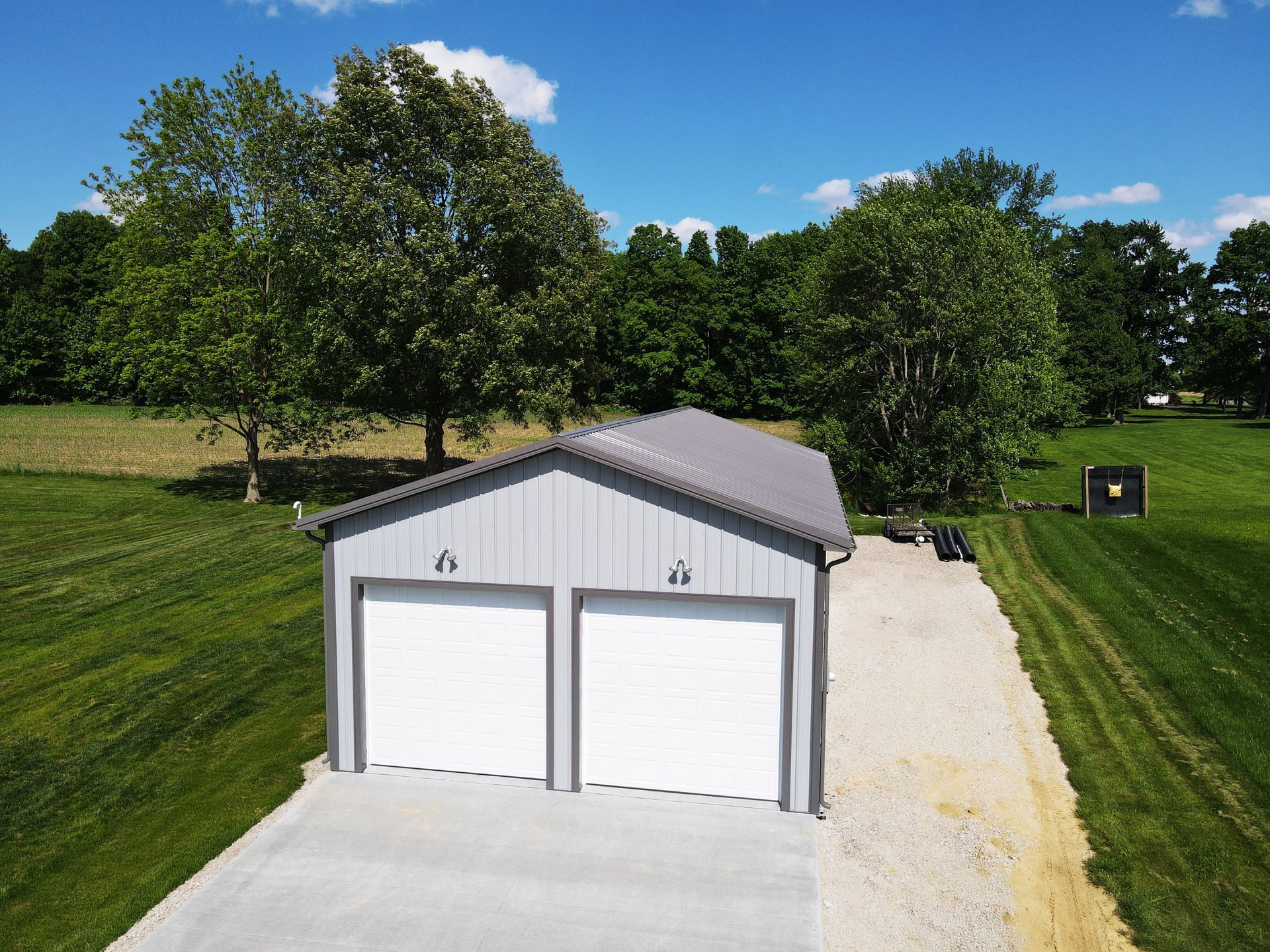 Two-car white garage with gray roof on a gravel driveway, surrounded by green trees and grass.