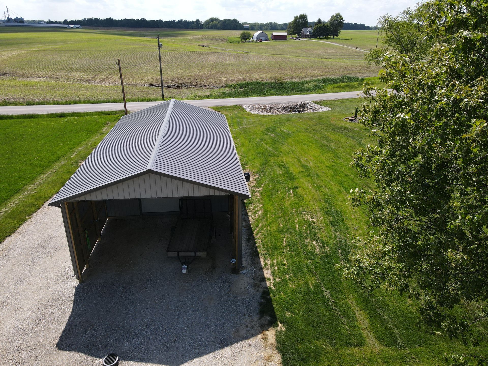 Small metal shed with a corrugated roof beside a grassy rural field, seen from above