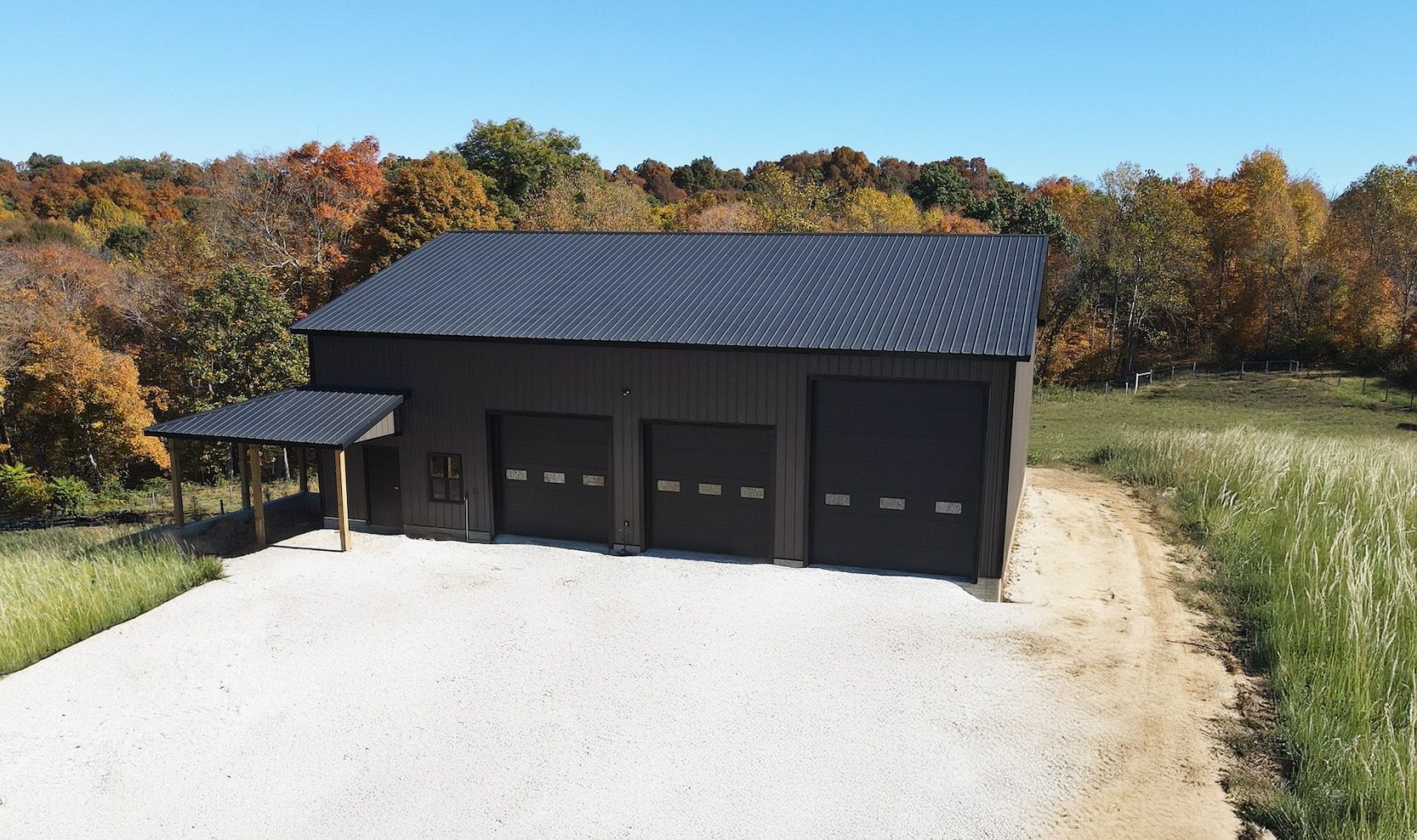 Detached black three-car garage with gravel driveway in a rural autumn setting