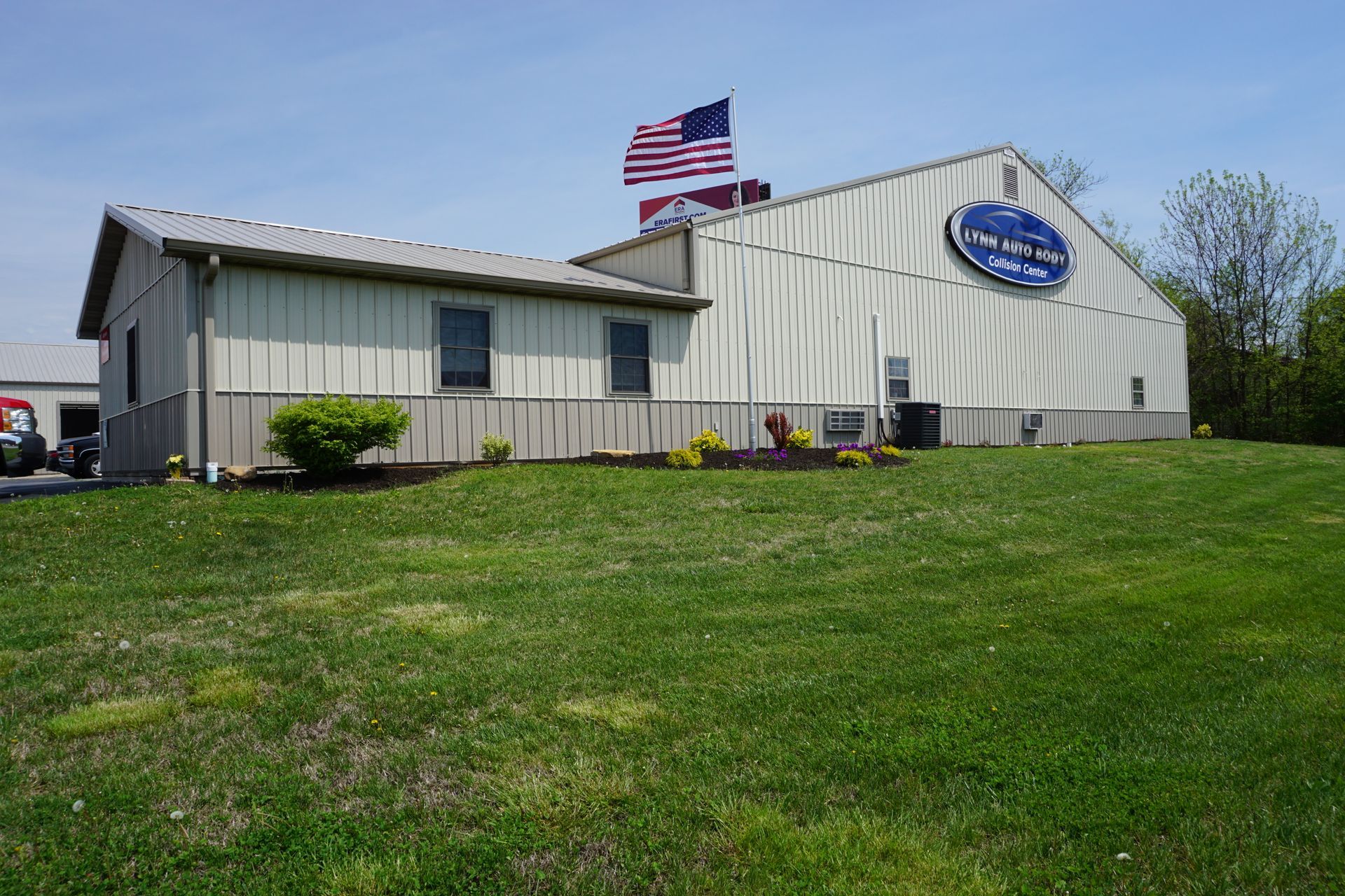 Small beige building with a blue sign and American flag on a grassy lawn under a clear sky