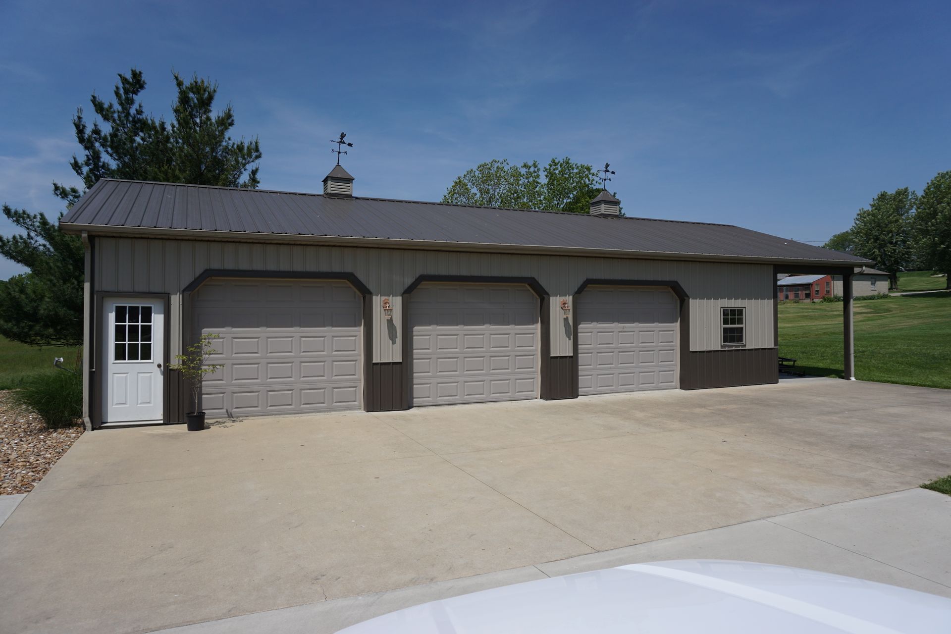 Three-bay garage with beige doors and gray siding beside a paved driveway on a sunny day