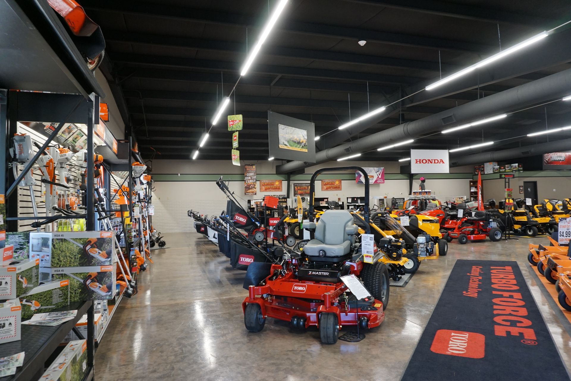 Indoor showroom with rows of lawn mowers and utility vehicles on display under bright lights
