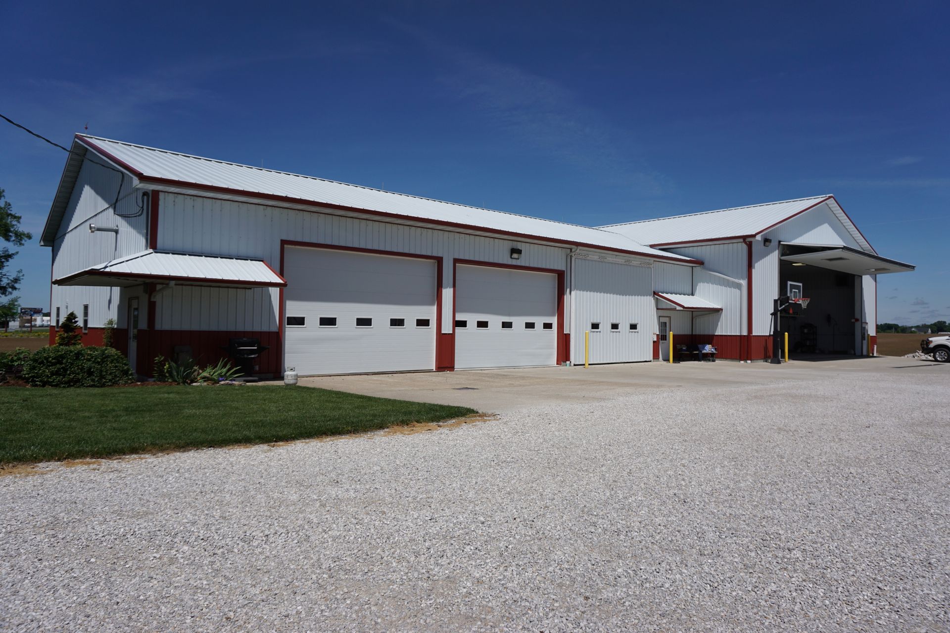 White barn-like building with large garage doors and gravel driveway under a blue sky