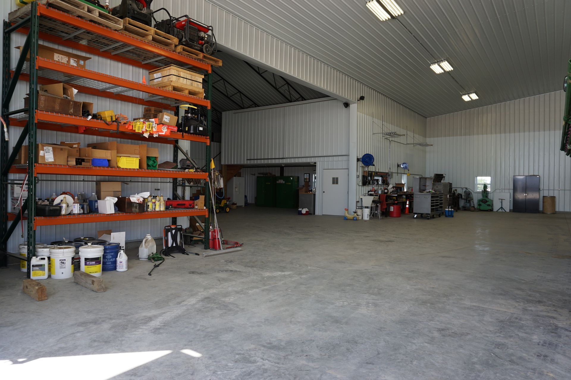 Large industrial workshop interior with metal shelving, tools, and equipment on a concrete floor.