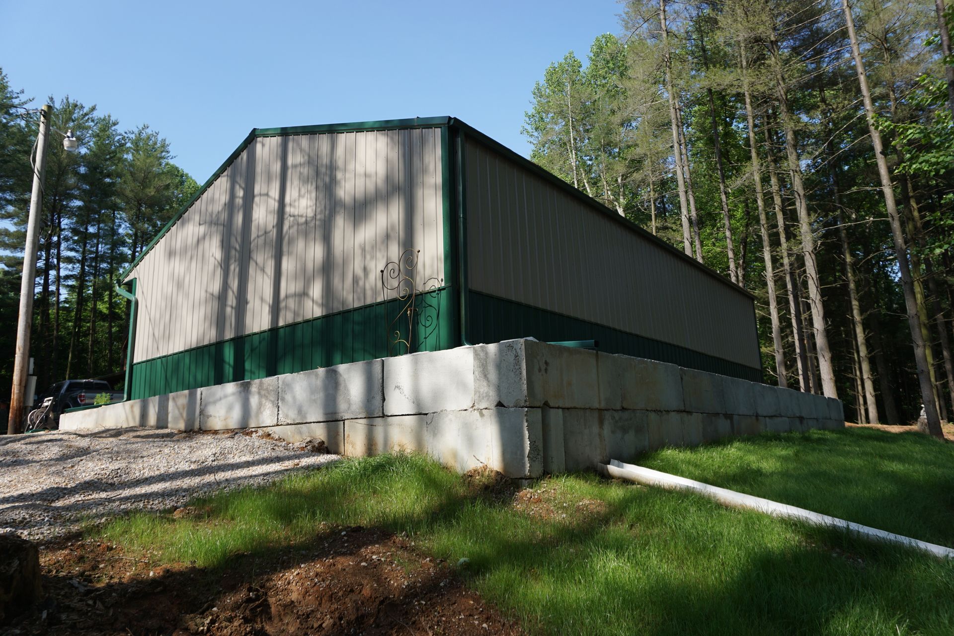 Large green-and-gray metal building on a concrete foundation in a wooded area