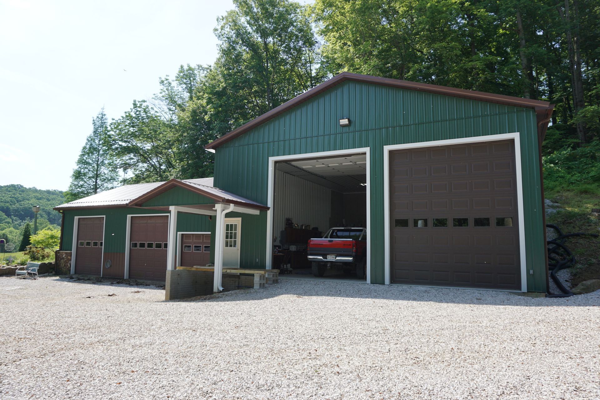 Green barn-style garages on a gravel lot, with a red pickup truck inside the open center bay.