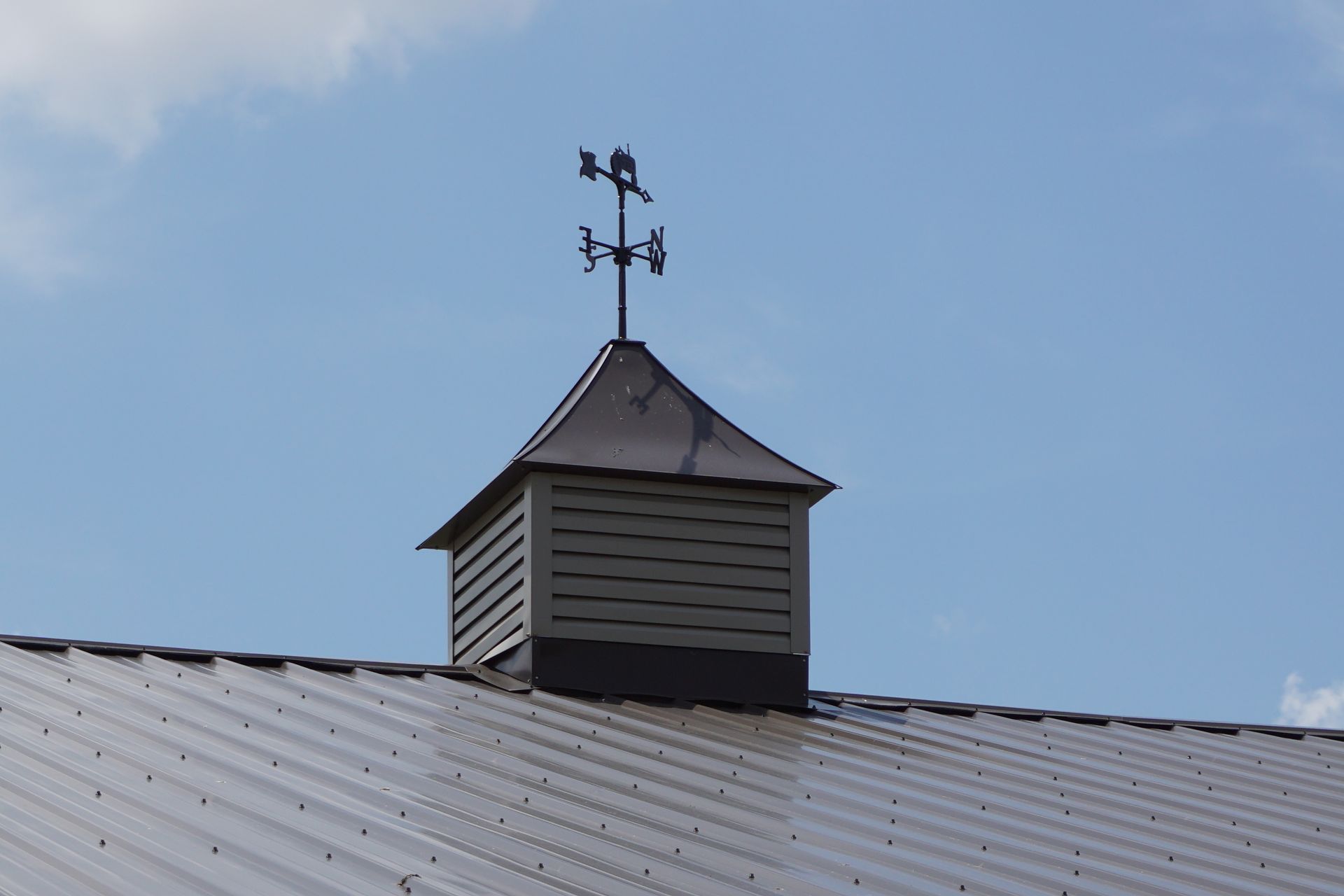 Metal roof with a small weather vane-topped cupola against a blue sky