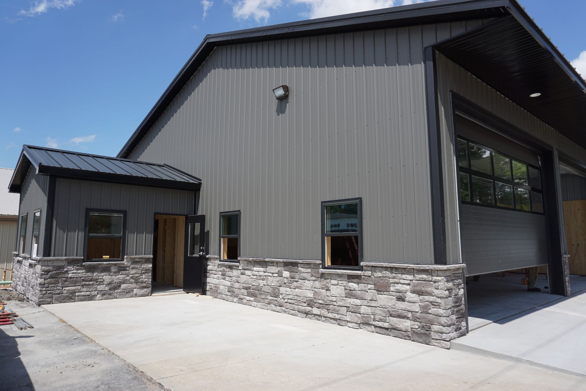 Modern gray building with stone base, large garage opening, and concrete driveway under a blue sky