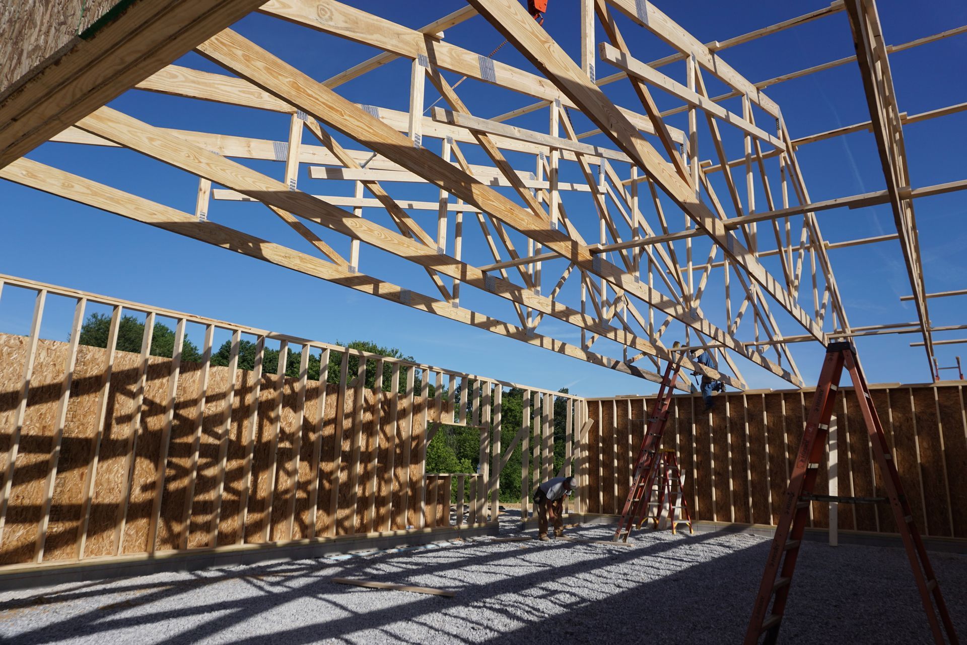 Wood-framed building under construction with exposed rafters and clear blue sky overhead
