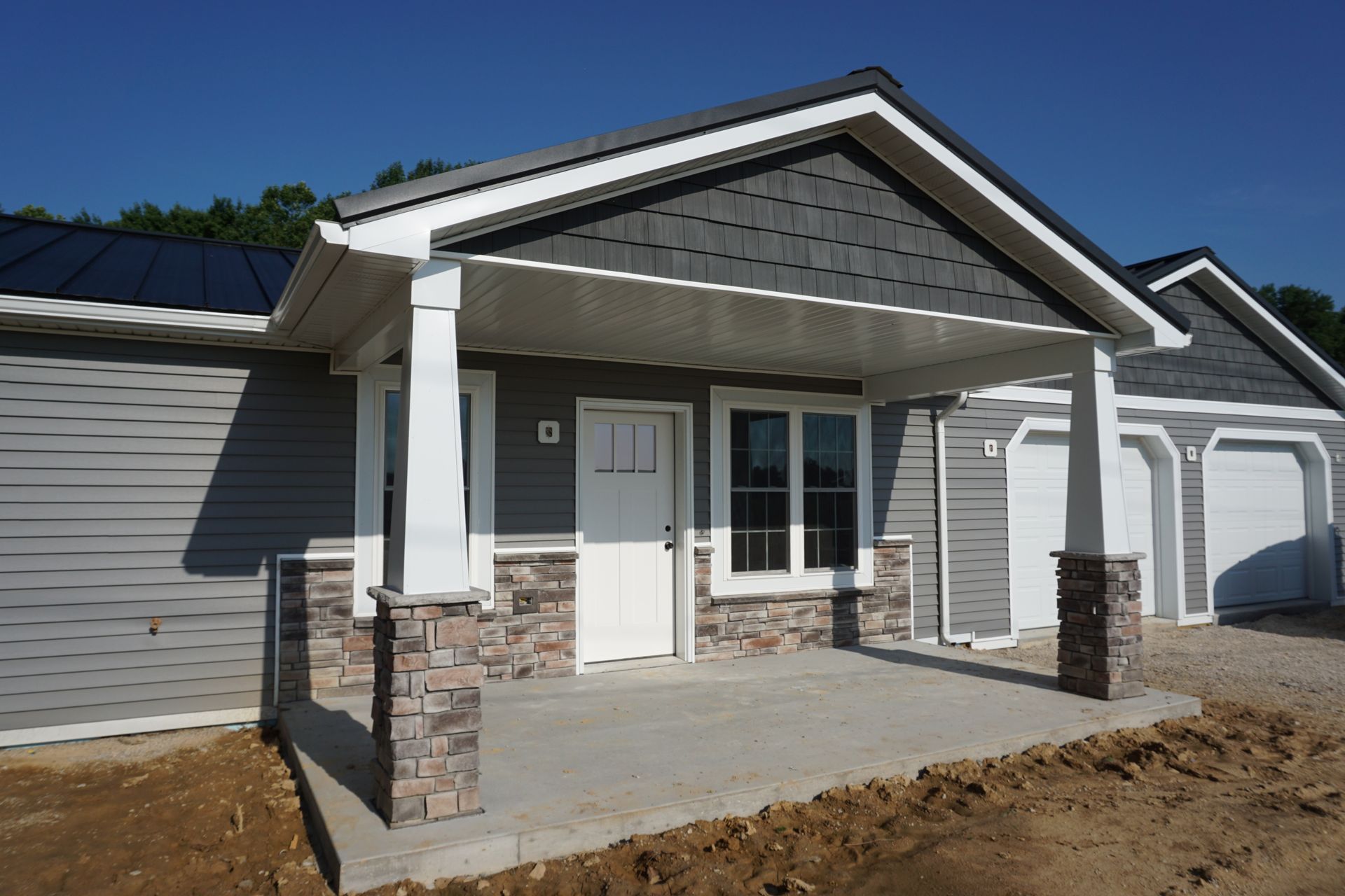 Front porch of a gray house with white trim, stone columns, and a small gabled roof over the entrance