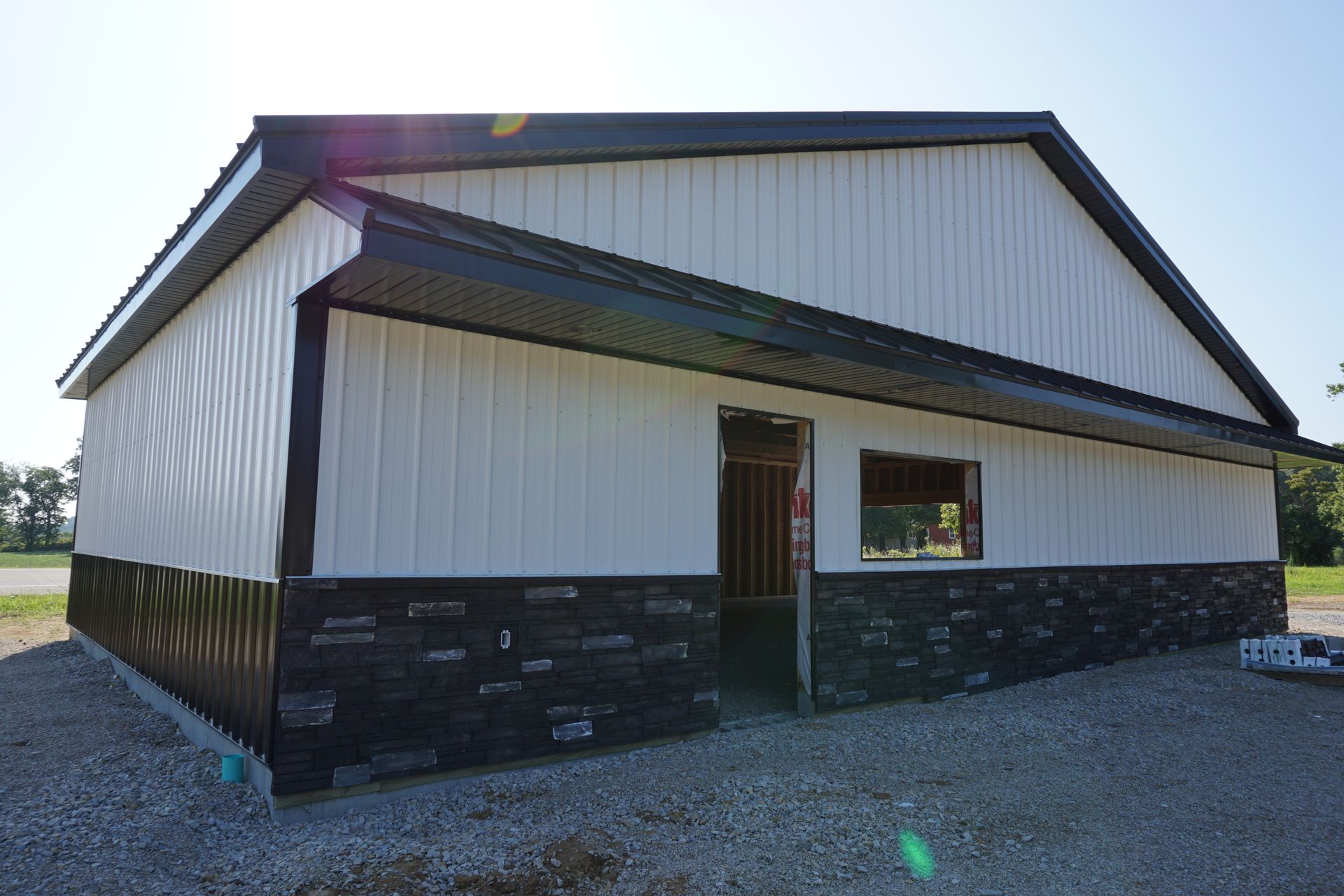 Small white-and-black building with a gabled roof on a gravel lot in bright sunlight