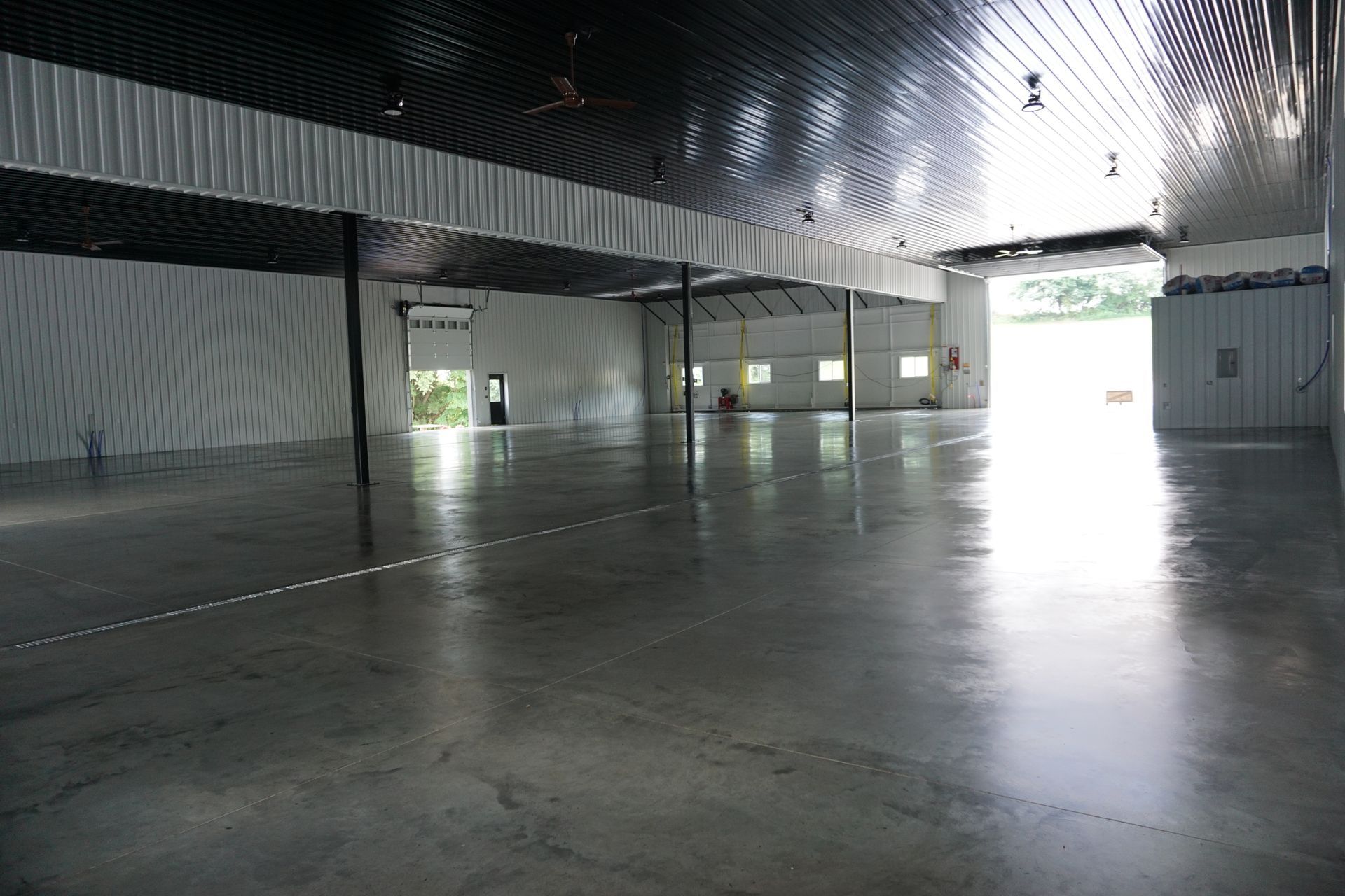 Empty industrial warehouse with polished concrete floor and bright open doors at the far end