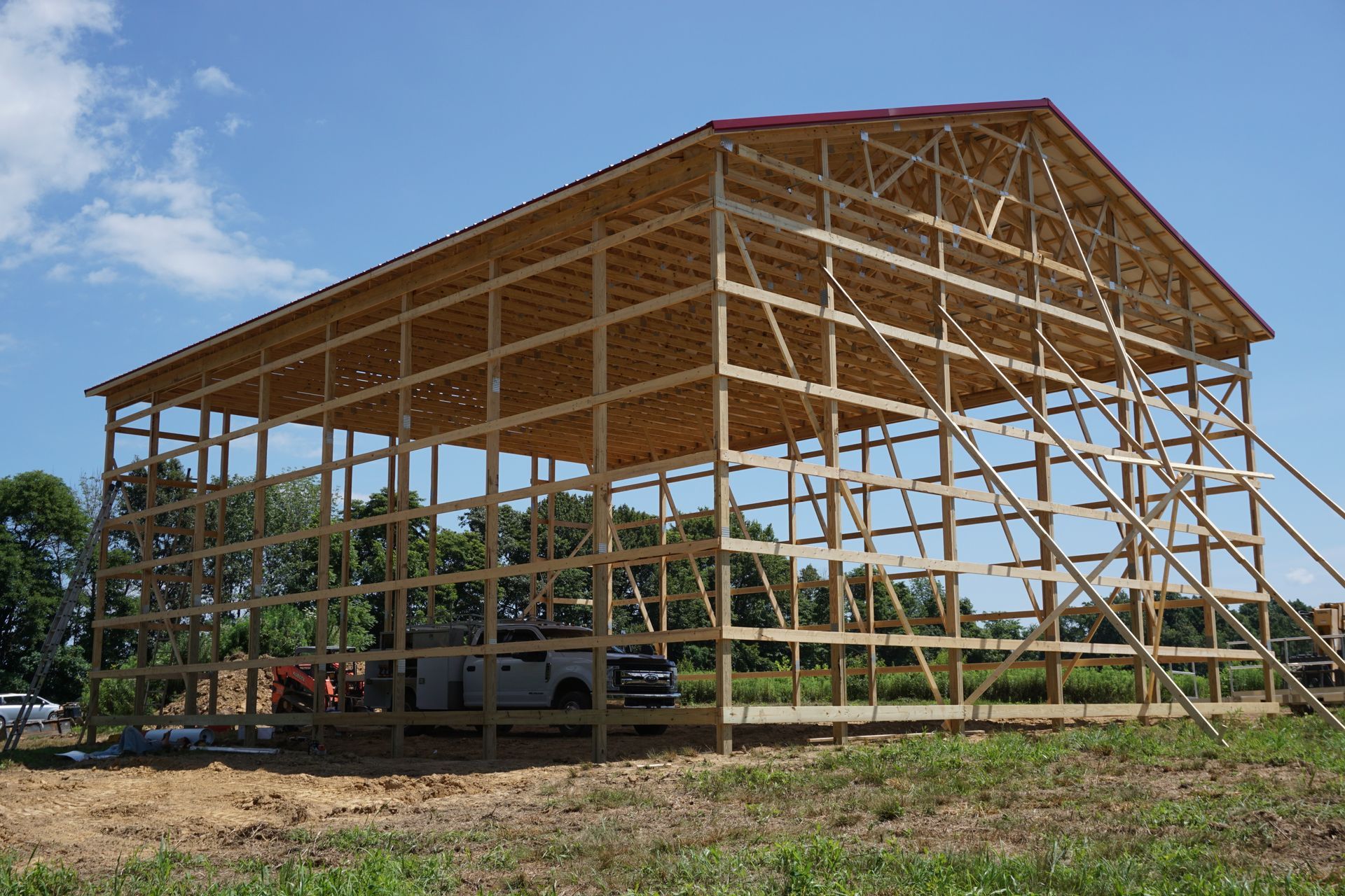 Partially built wooden barn frame with roof trusses in a rural field under a blue sky