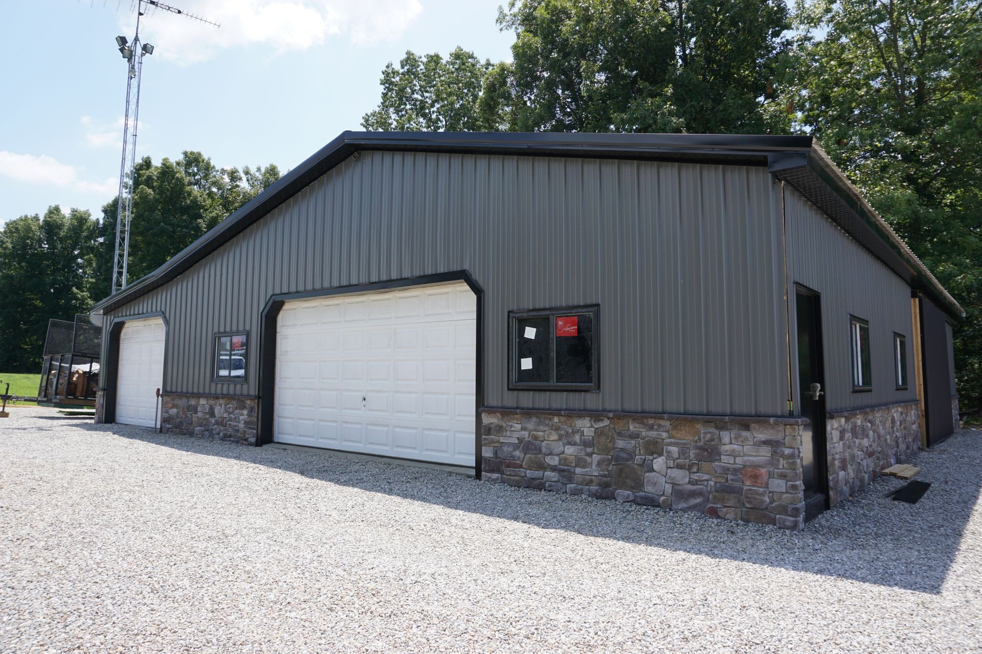 Gray metal garage building with two white doors and stone base on a gravel lot.