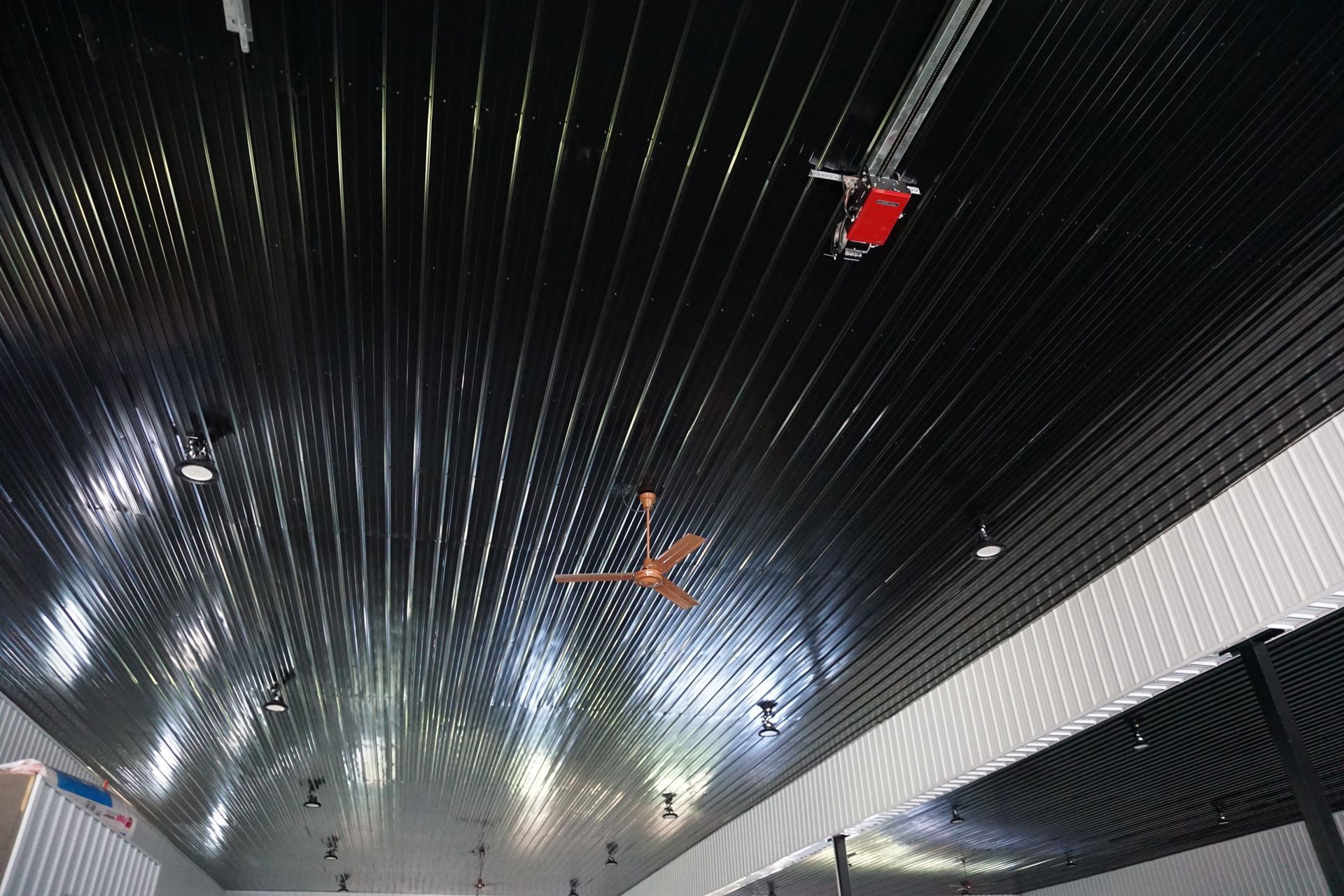Ceiling view of a modern interior with dark slats, bright lights, and small red and orange hanging figures