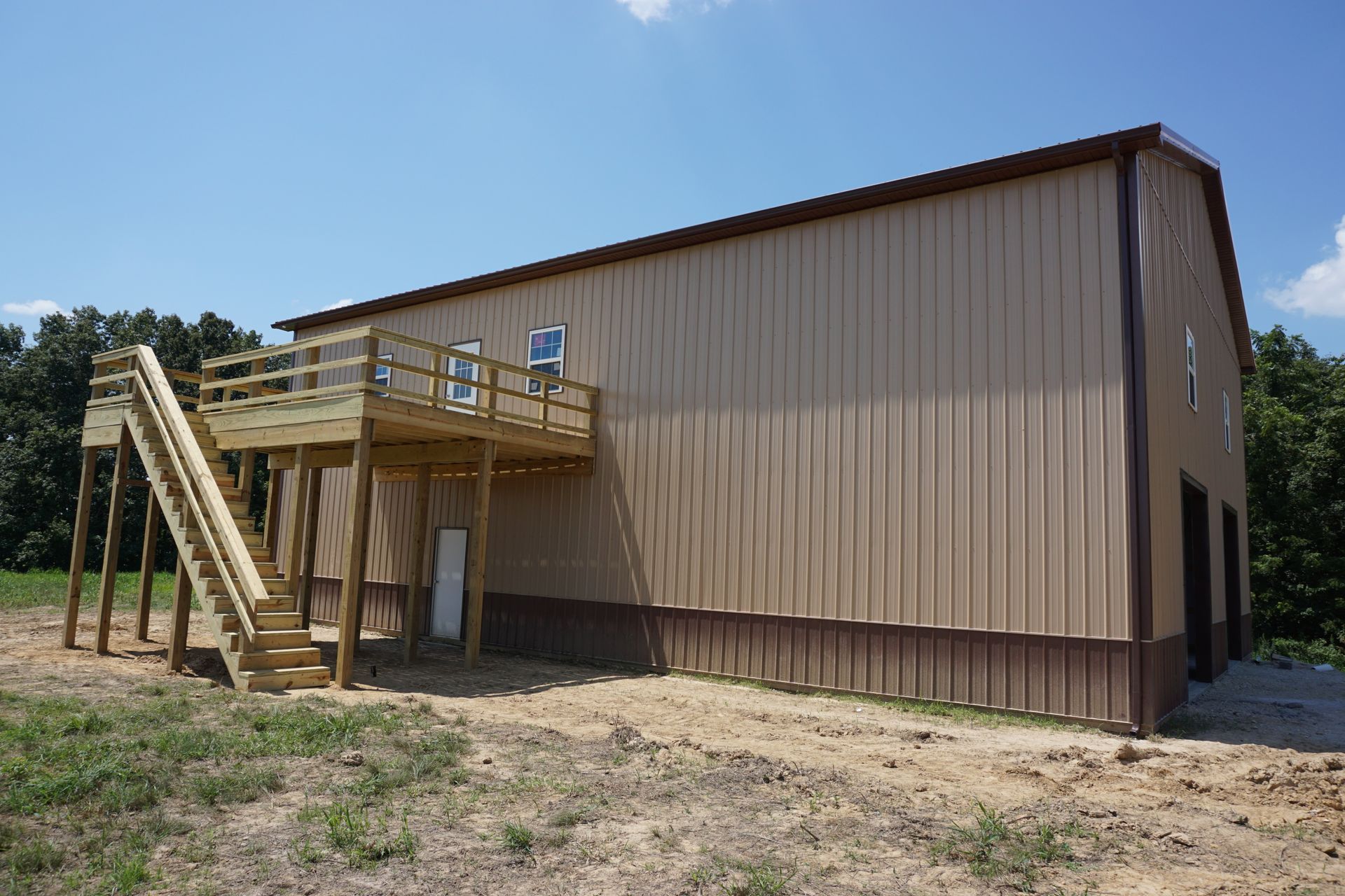 Tan metal-sided building with an exterior wooden staircase and deck on a dirt lot.