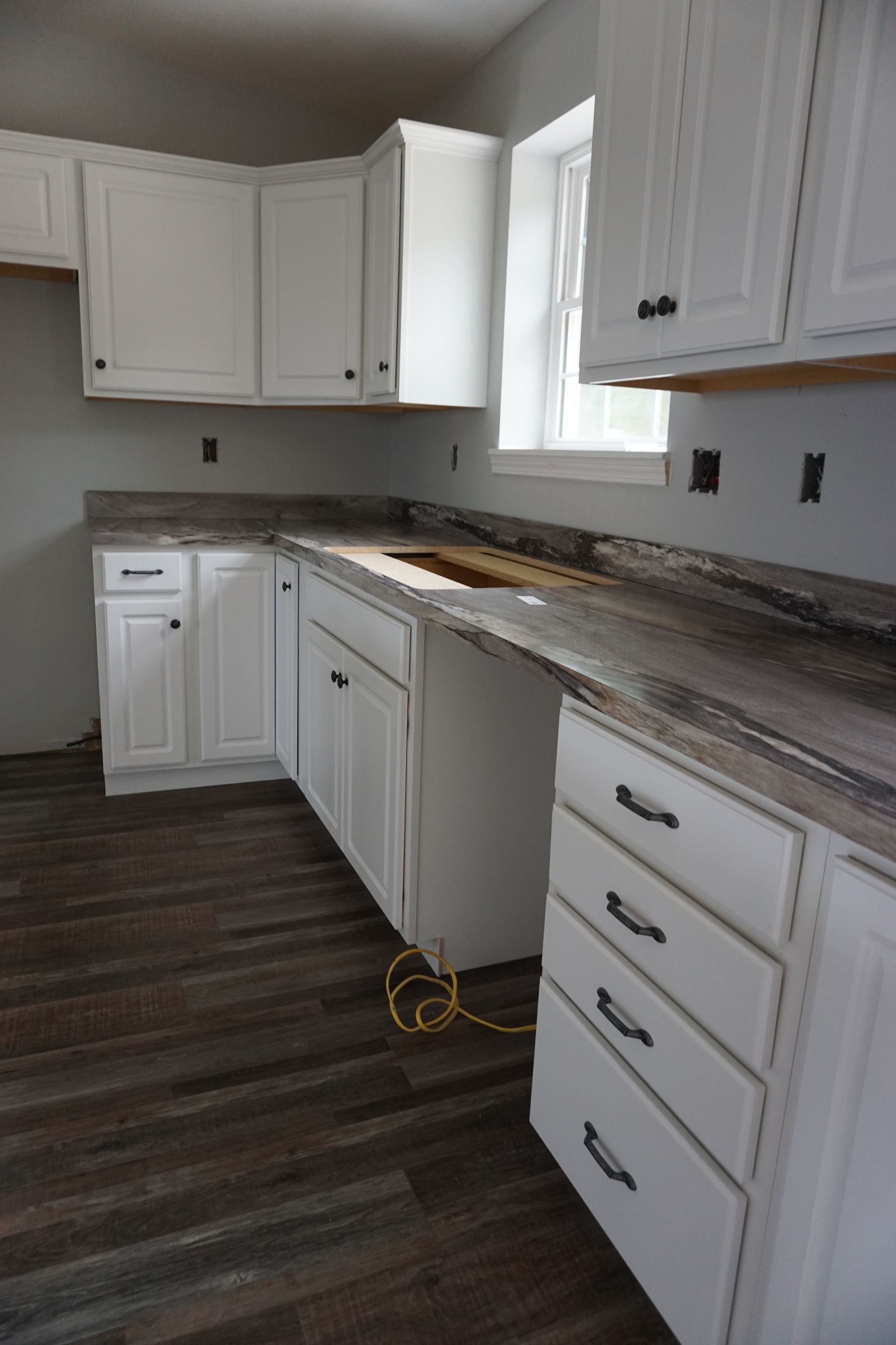 Unfinished white kitchen with cabinets, countertops, and dark wood floor, showing renovation work.