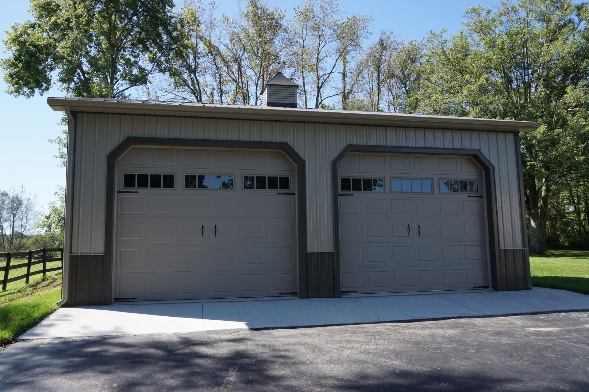 Two gray garage doors on a beige detached garage with trees and a driveway in front