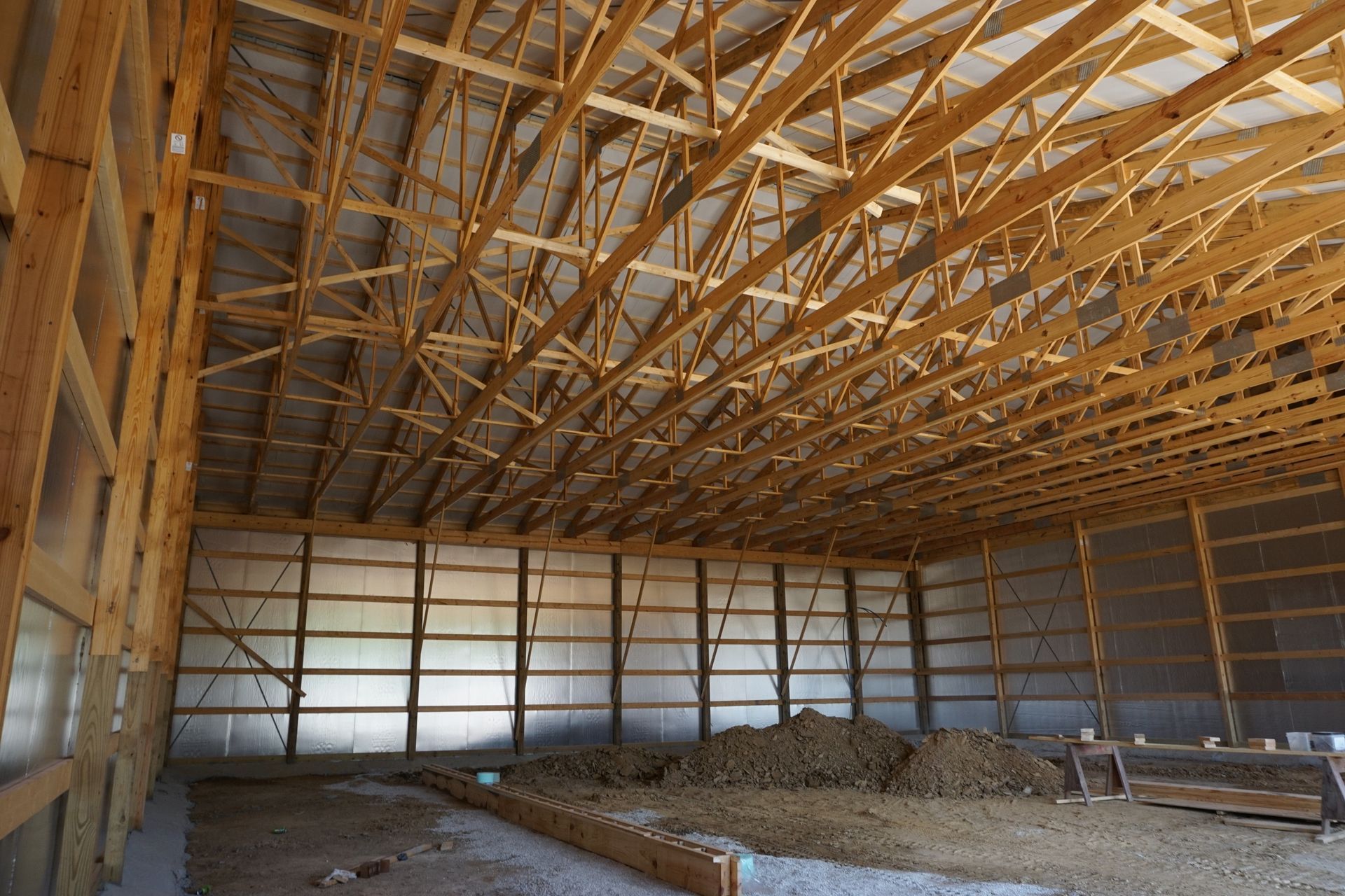 Interior of unfinished barn with exposed wooden roof trusses and gravel floor