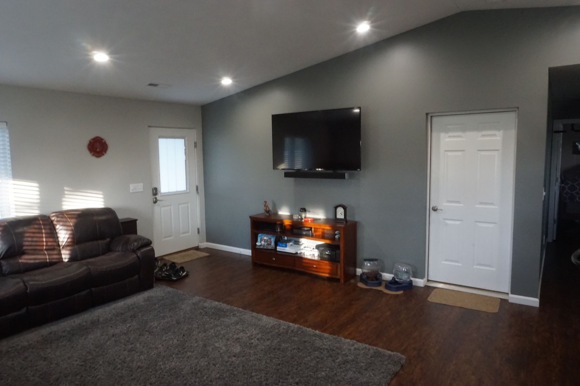 Living room with dark sofa, wall-mounted TV, electric fireplace, and gray rug on hardwood floor