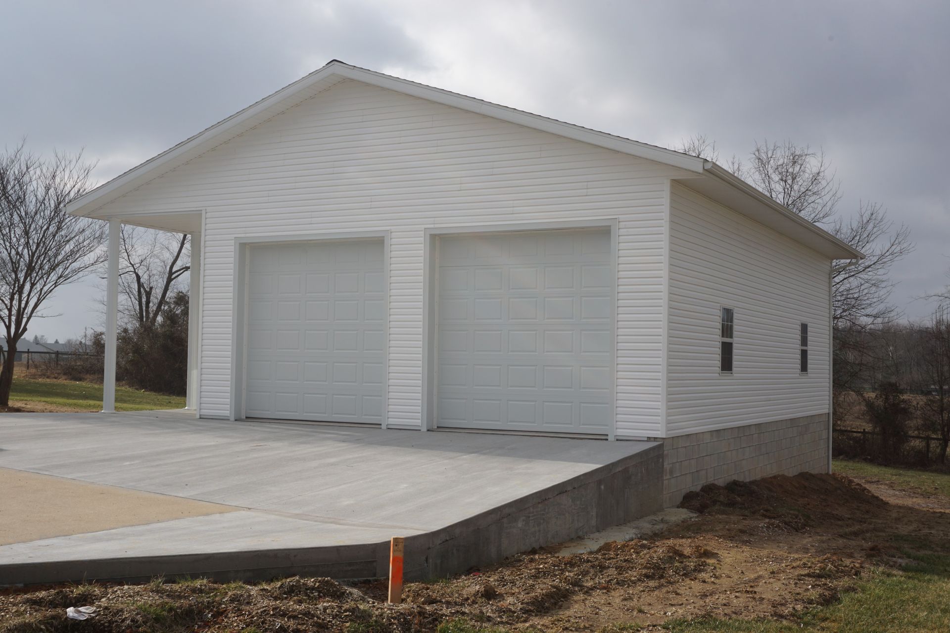 White detached garage with two doors and a concrete driveway under an overcast sky