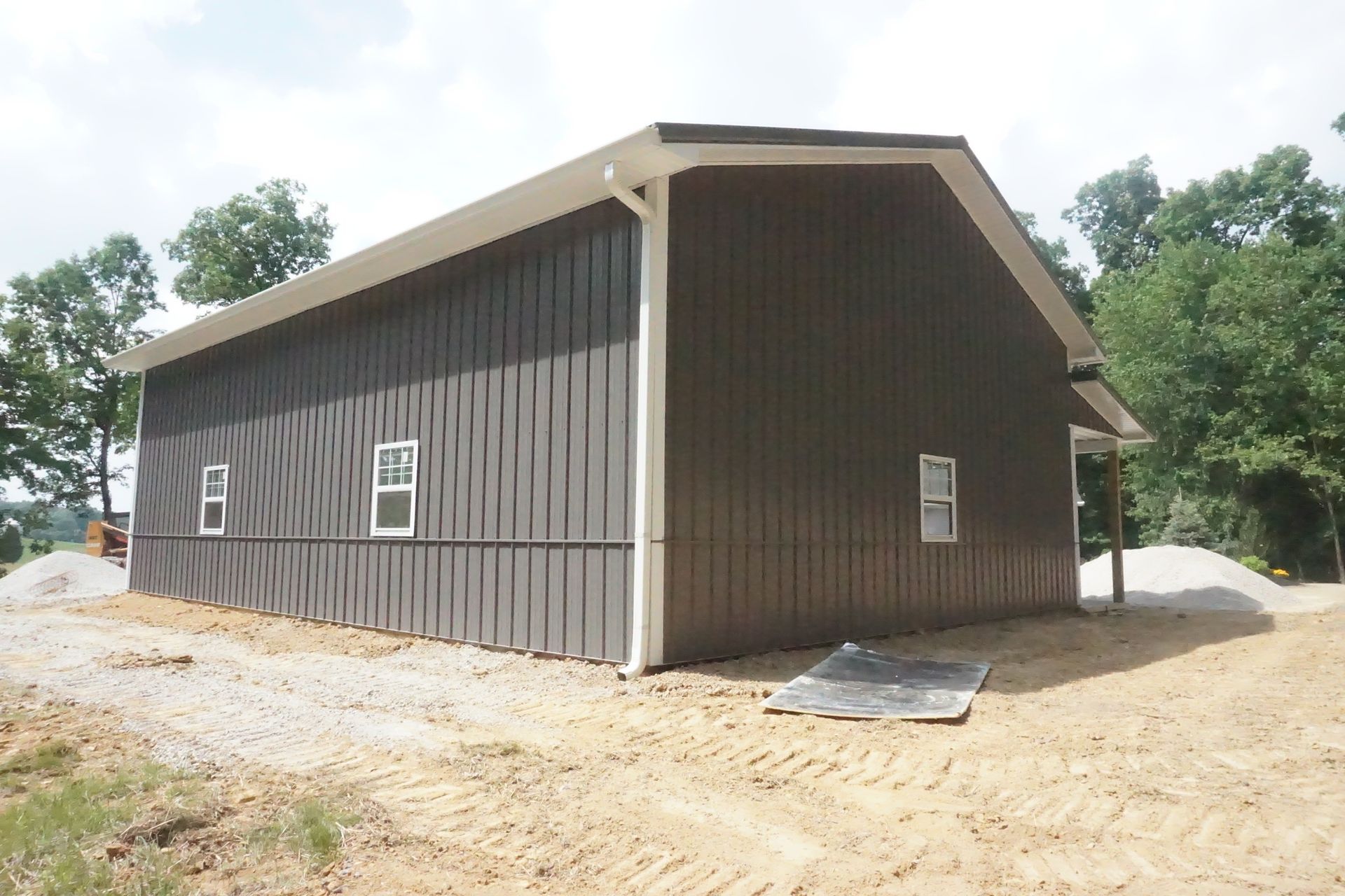 Brown wooden barn-like building on a dirt lot with white trim and small windows under a cloudy sky