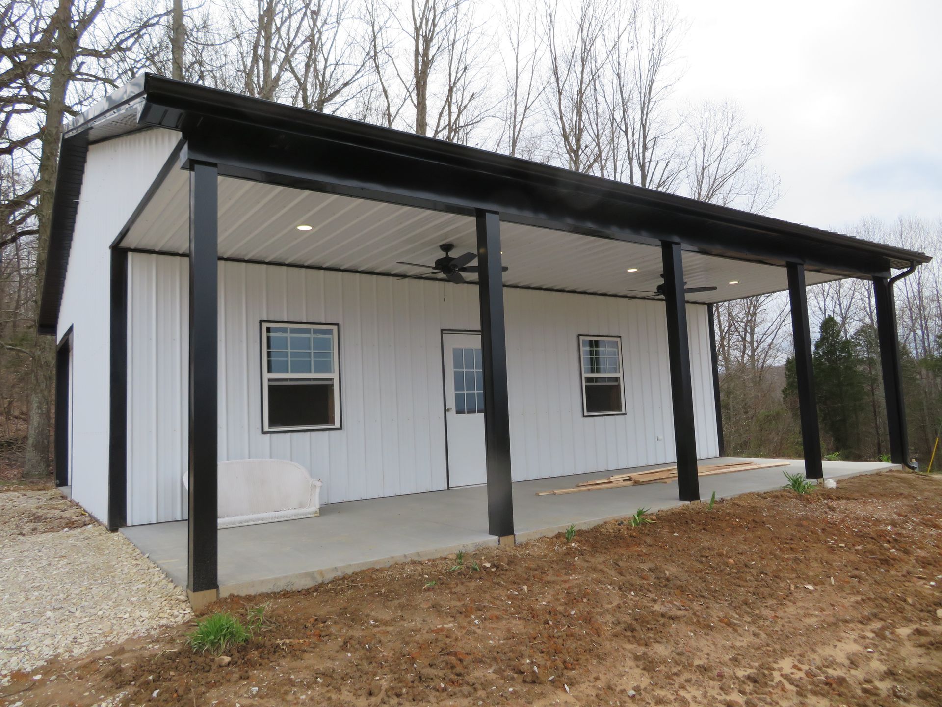 Small white building with a covered porch and black posts on a dirt lot