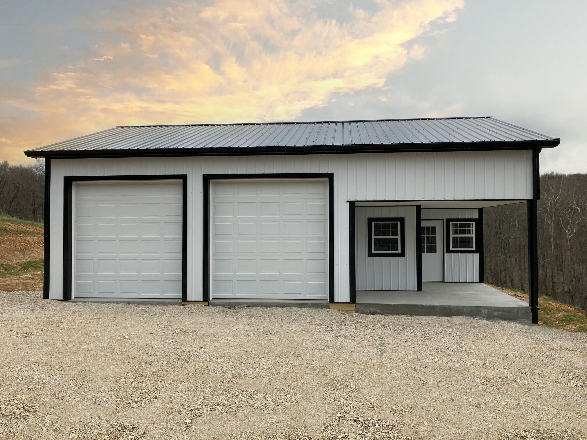 White metal garage with two doors and a small side entrance on a gravel lot at sunset.