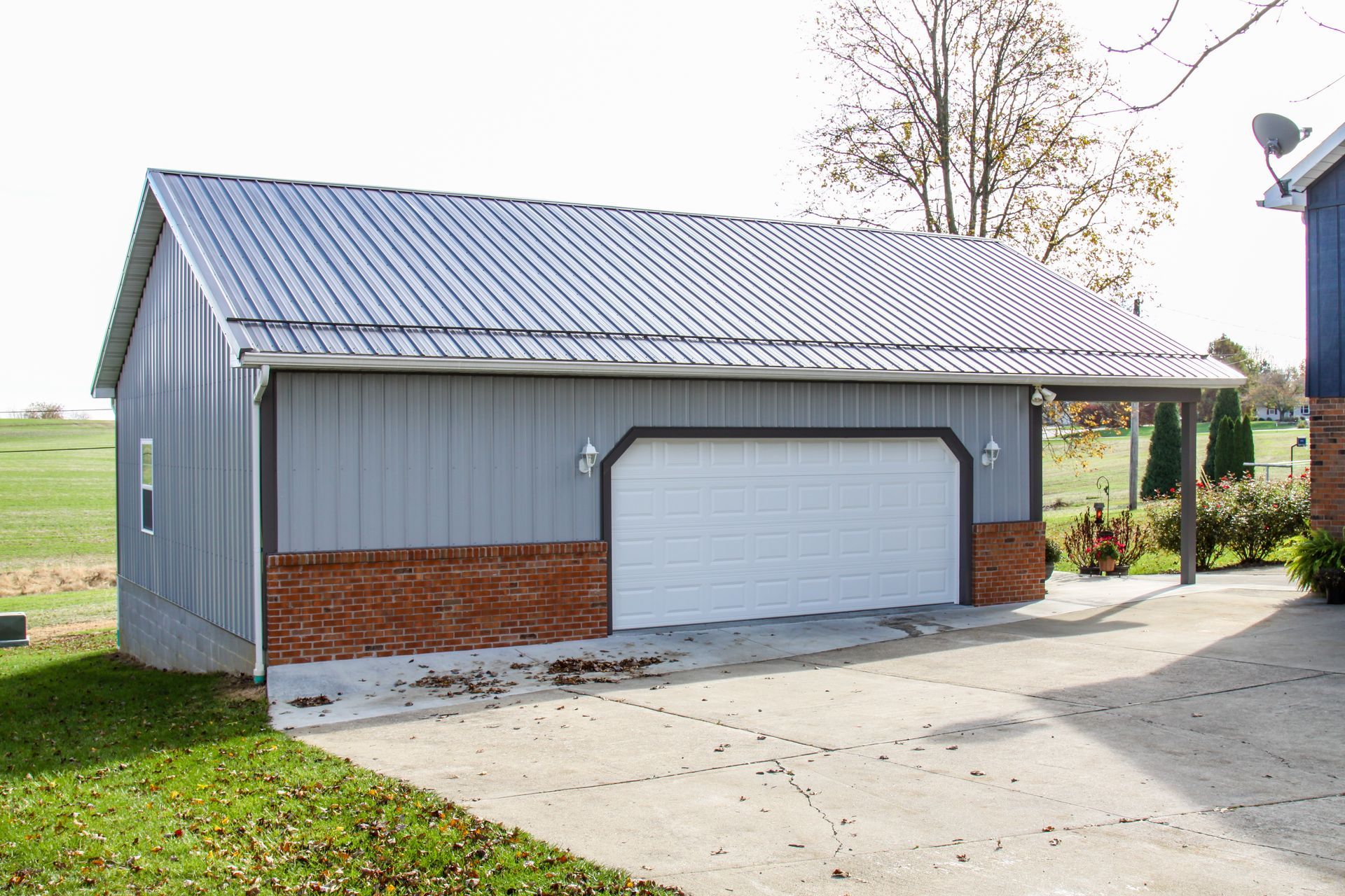 Gray detached garage with metal roof and white door beside a driveway and lawn