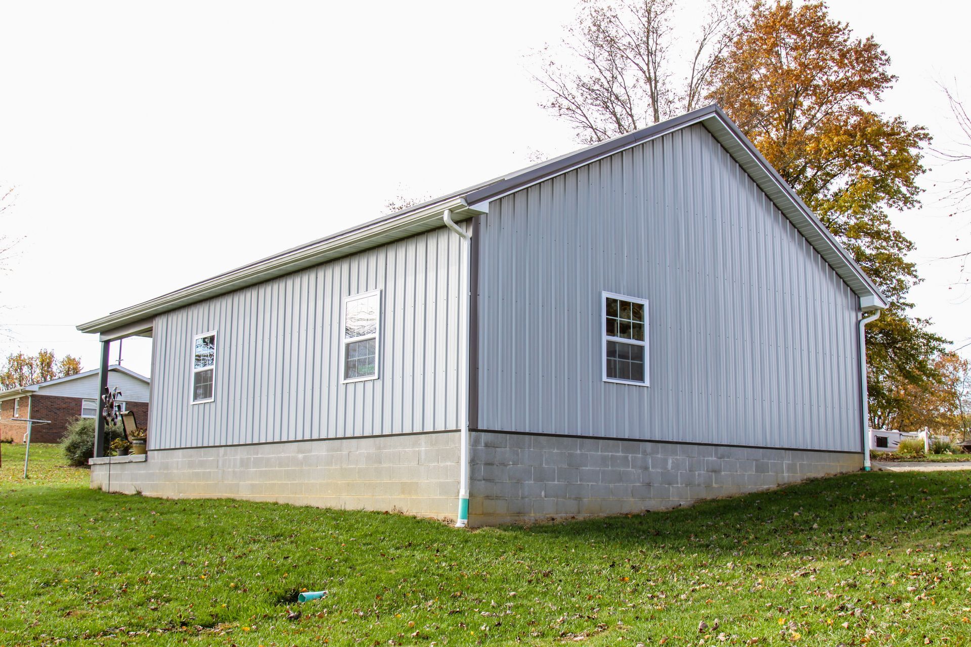 Gray metal shed with white doors on a concrete foundation in a grassy yard, with trees behind it