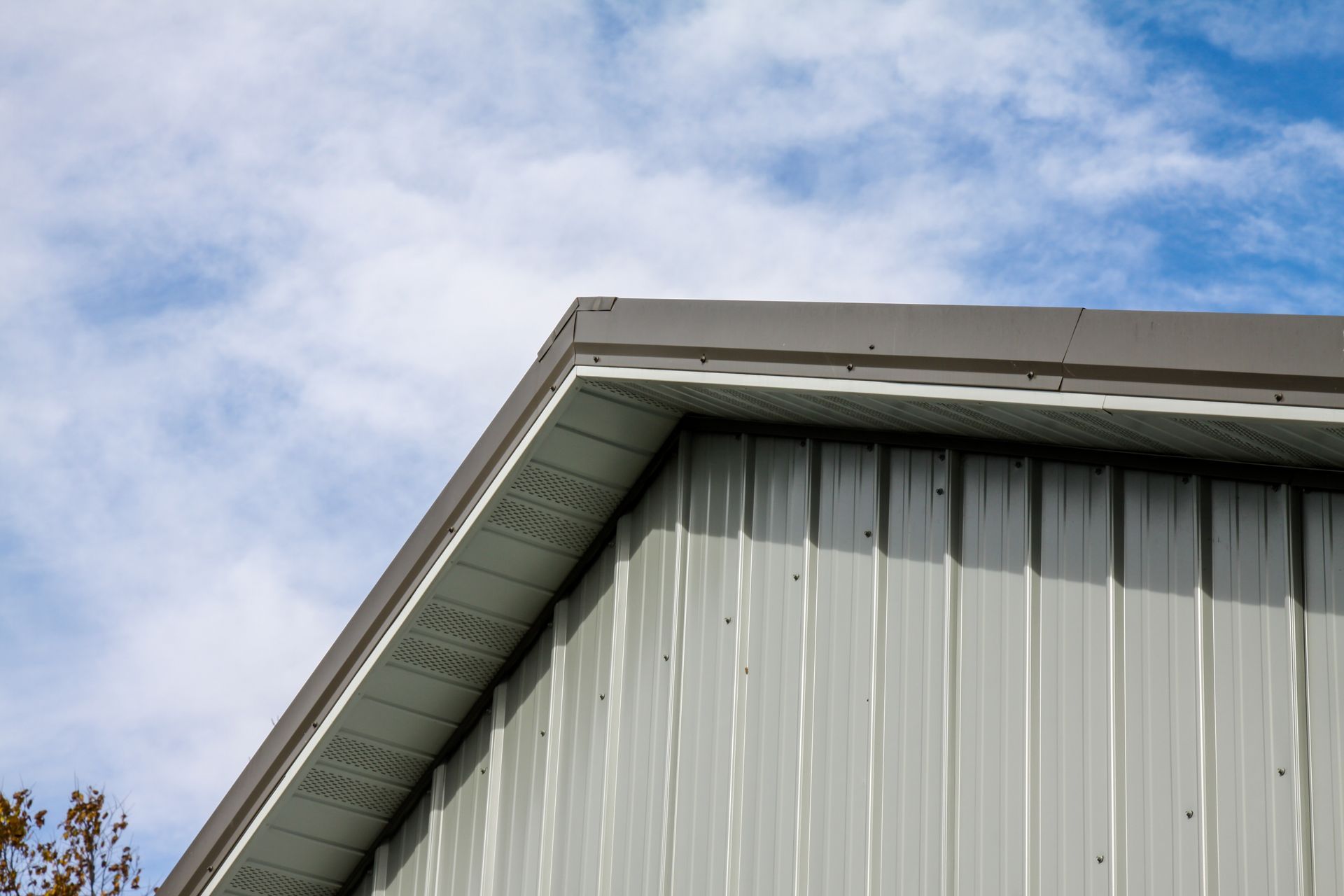 White metal building roofline against a blue, cloudy sky