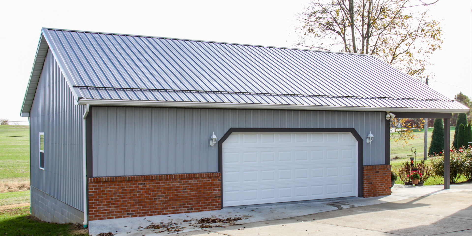 Gray metal garage with white roll-up door and brick trim on a rural property