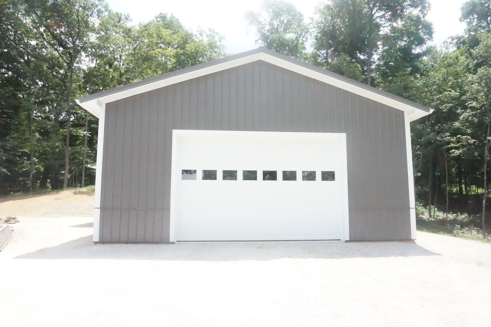 Gray garage or storage building with a white roll-up door surrounded by trees
