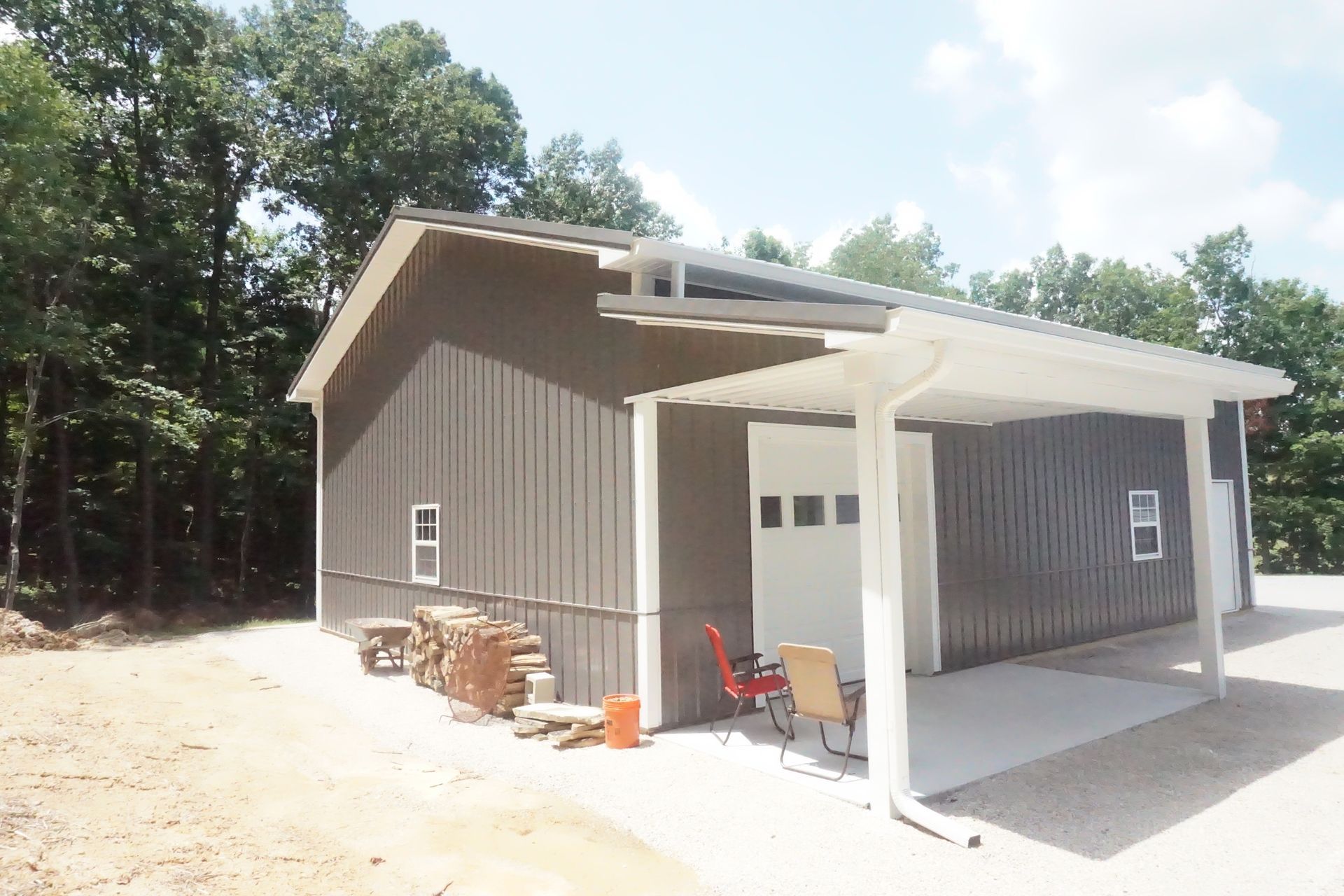 Gray detached garage with white trim, double doors, and a small covered porch in a wooded clearing