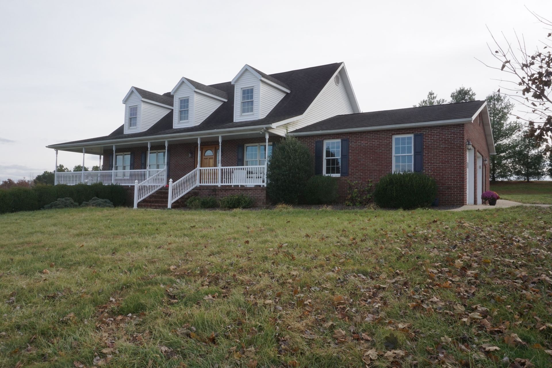 Large brick house with white dormers and a covered porch on a grassy hill