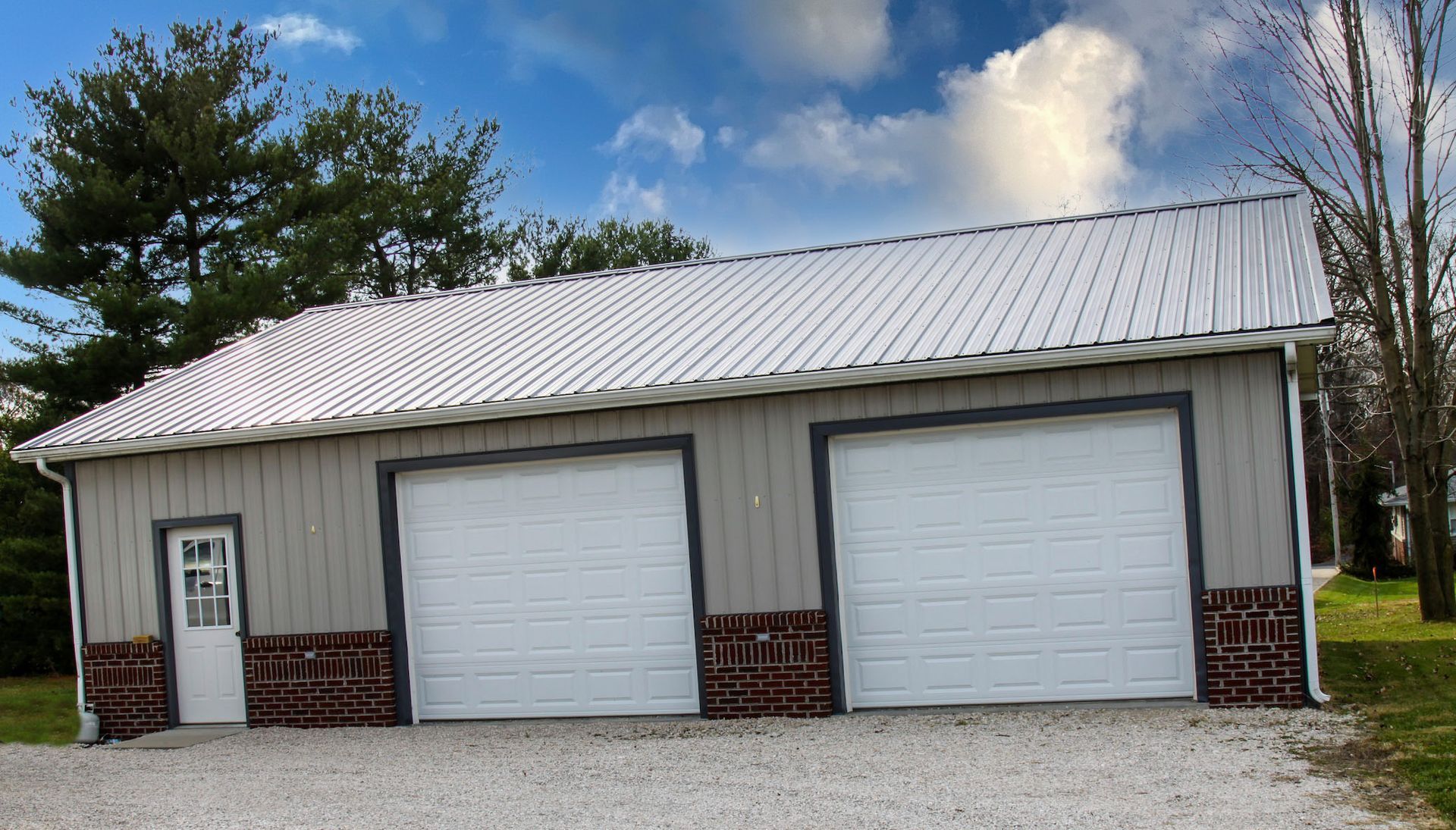 White metal garage with two roll-up doors and a side entry door under a cloudy sky
