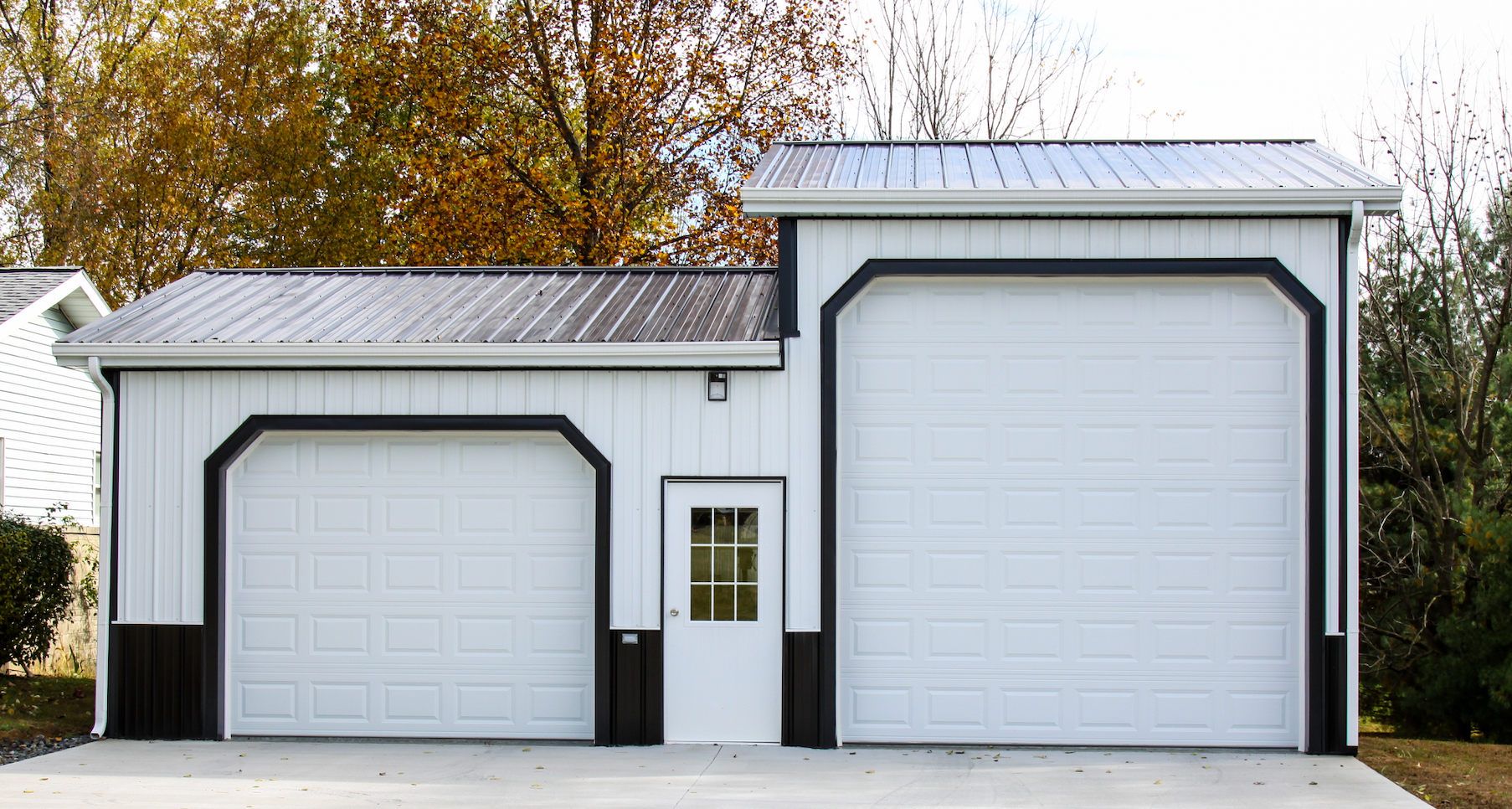 White garage with two doors, a small entry door, and autumn trees in the background