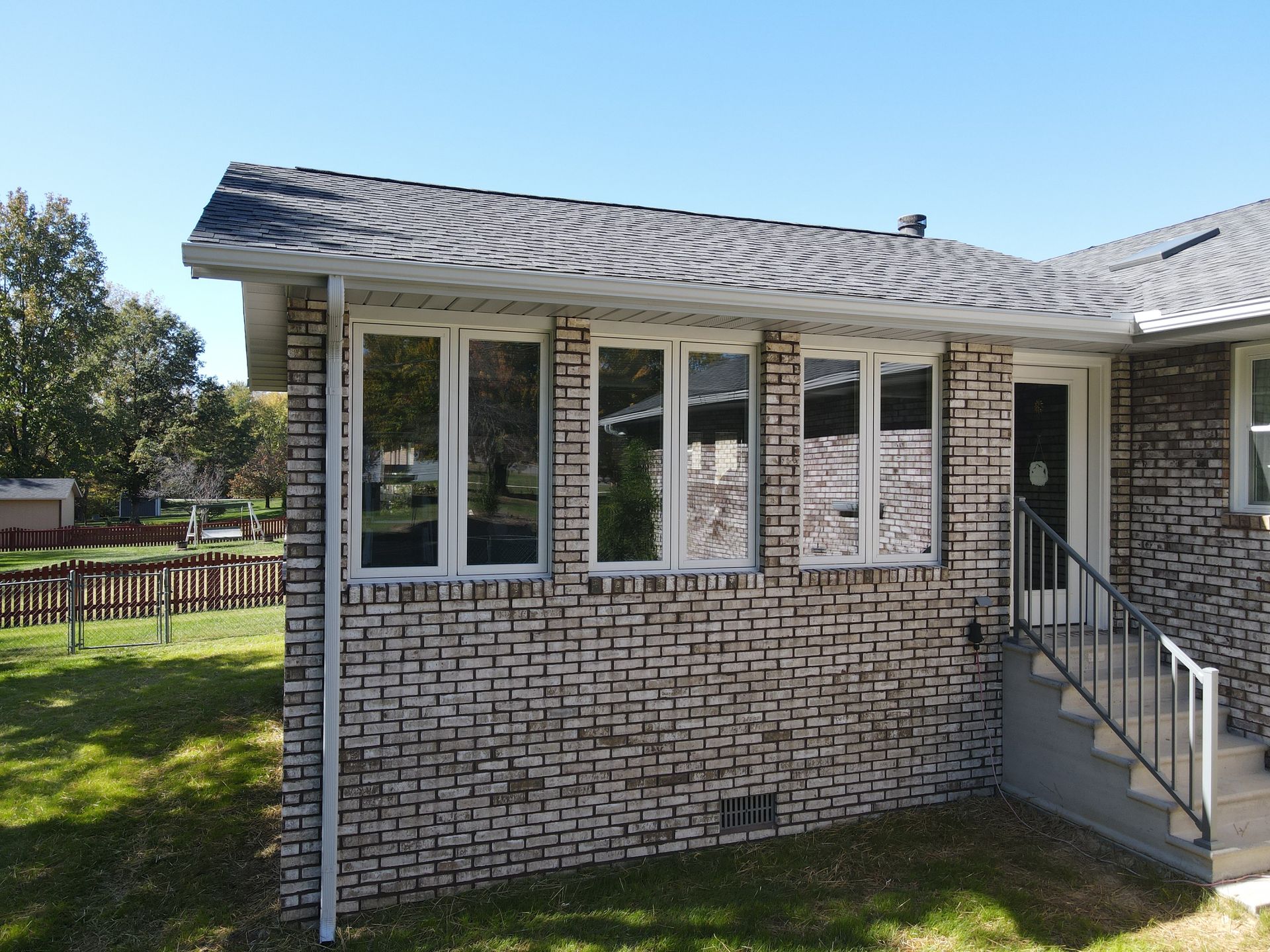 Brick house exterior with large front windows, a porch railing, and steps leading to the entrance