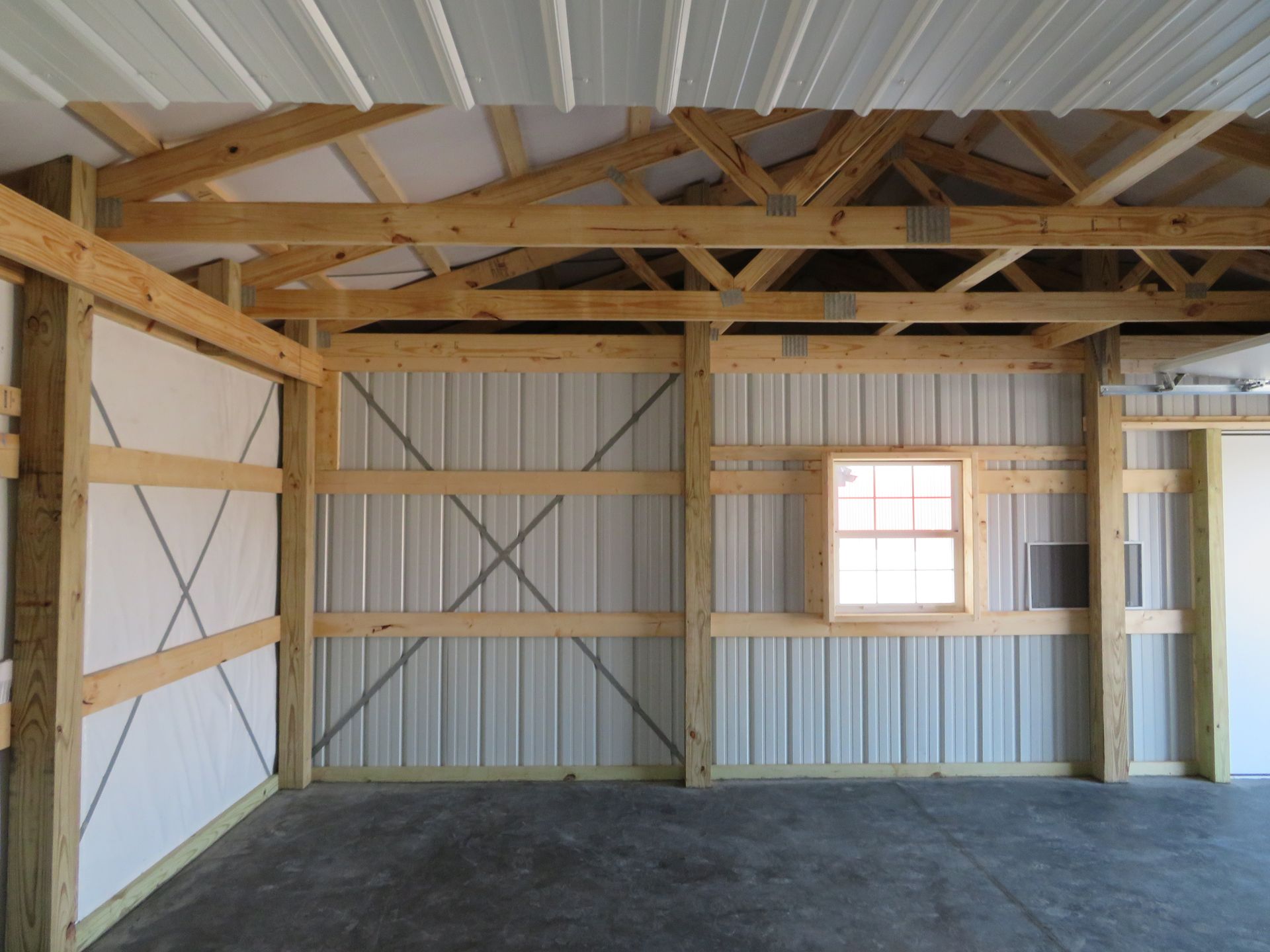 Empty unfinished garage with exposed wooden framing and corrugated metal walls, plus a small window.