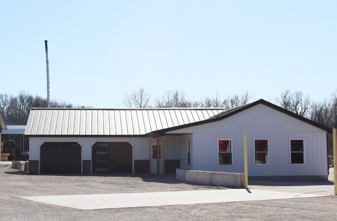 White industrial building with garage doors and a metal roof on a sunny day
