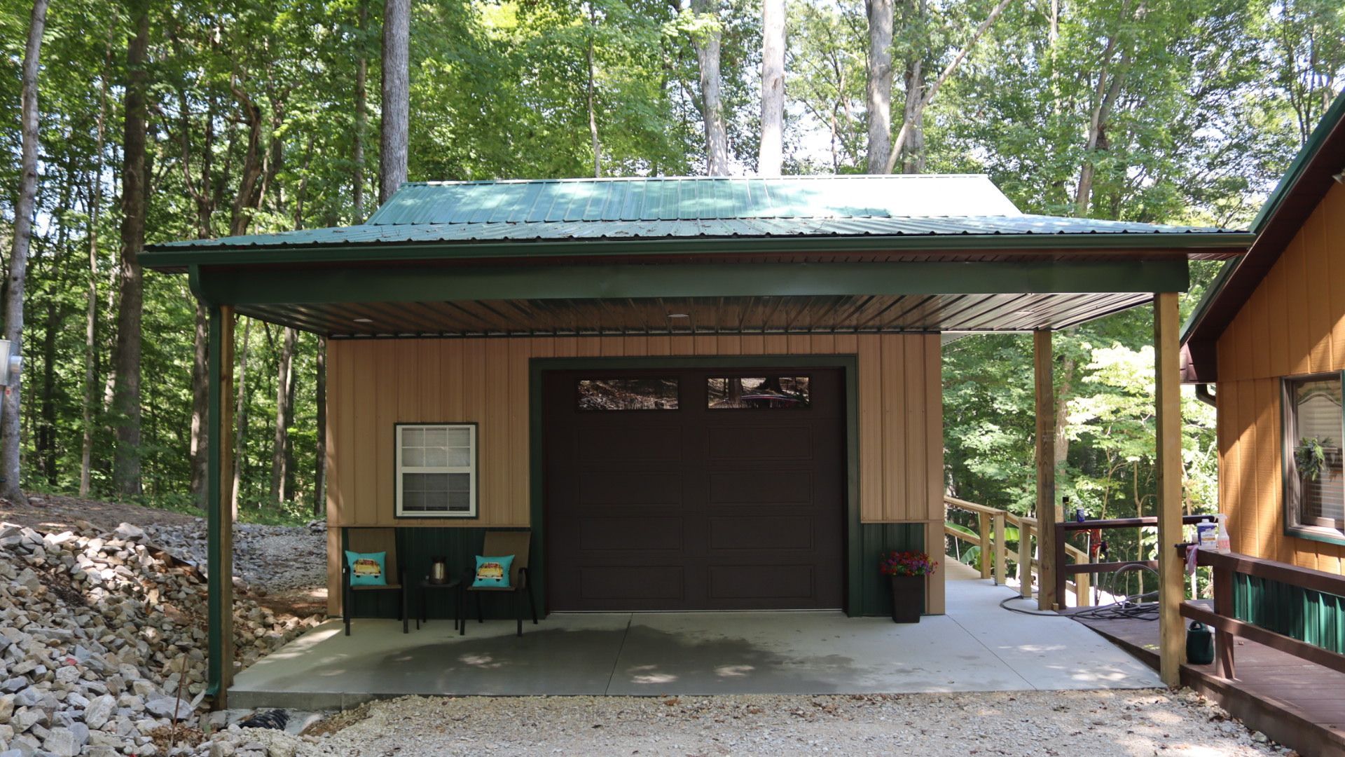 Small brown cabin with green roof and garage door in a wooded area