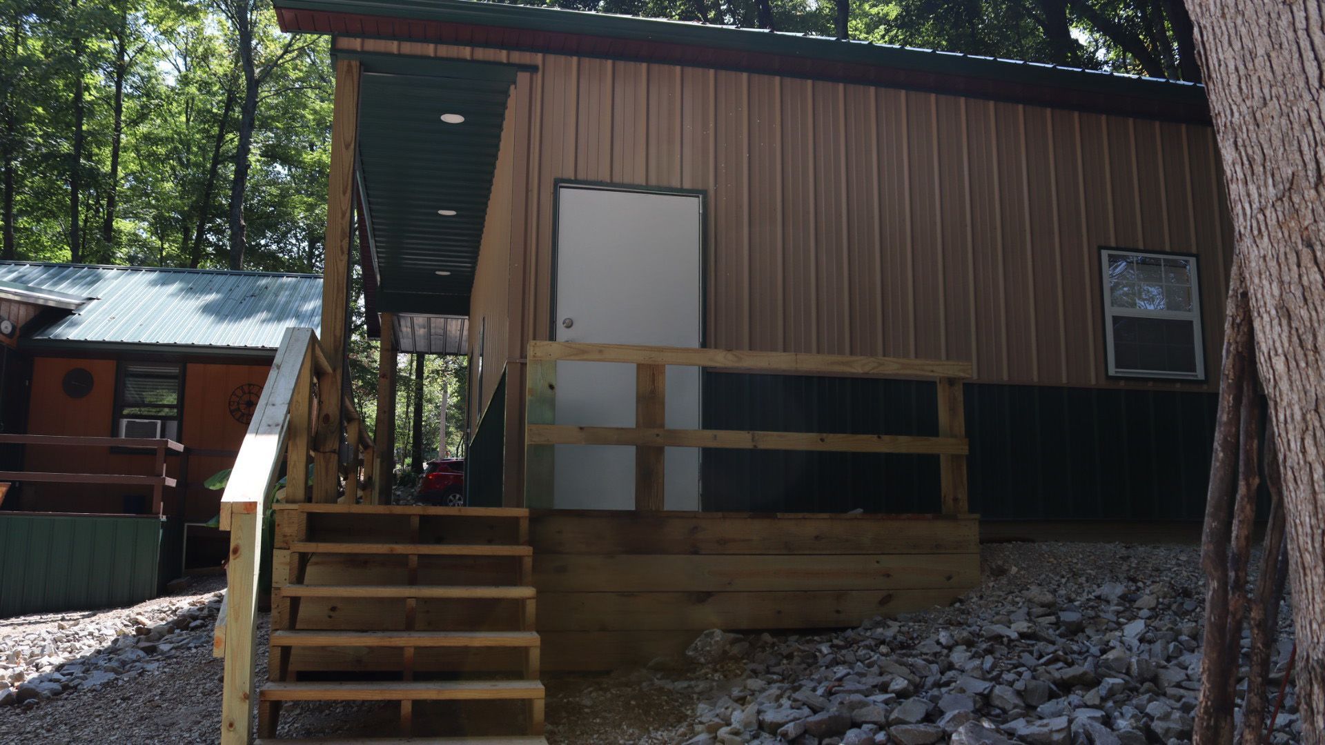 Small brown cabin with a front porch, stairs, and a white door in a wooded setting