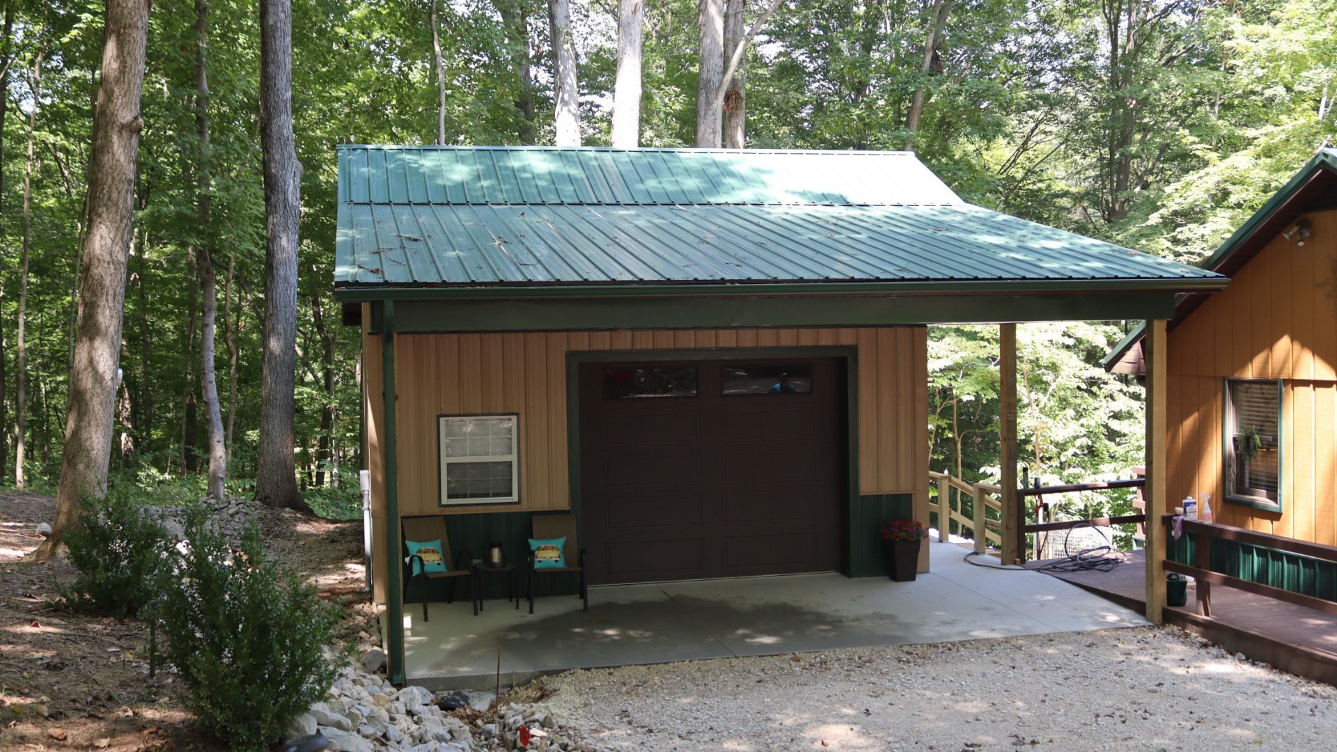 Small wooden cabin with green metal roof and open garage door in a wooded area