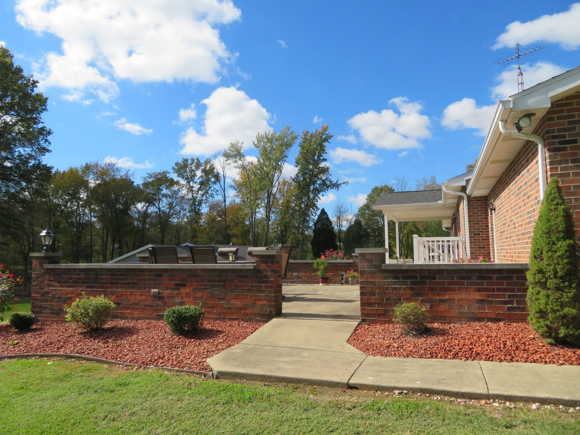 Backyard patio with brick retaining walls, concrete walkway, and a blue sky with clouds