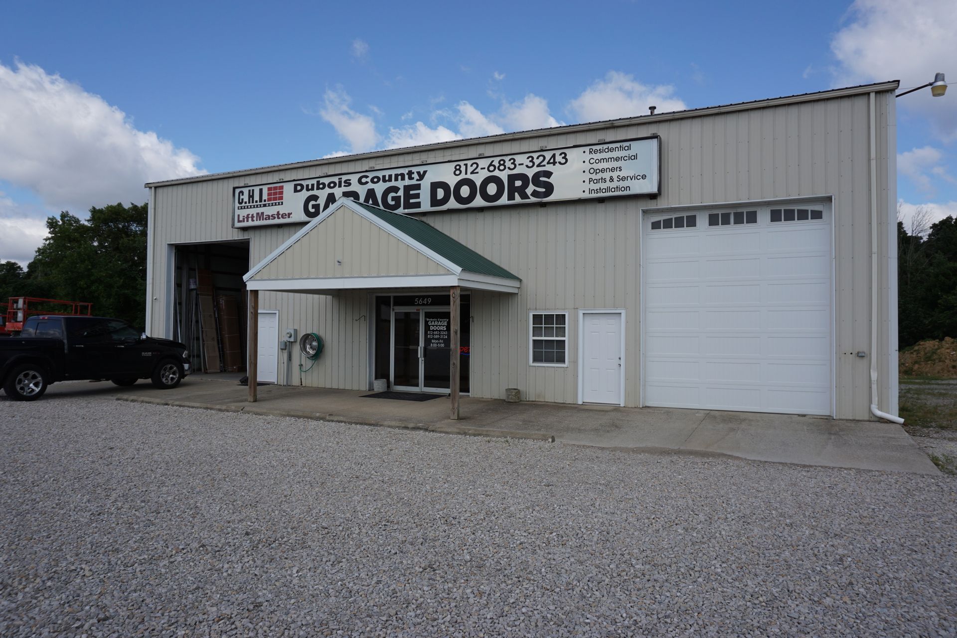 Exterior of a beige garage door business with a white awning and gravel parking lot