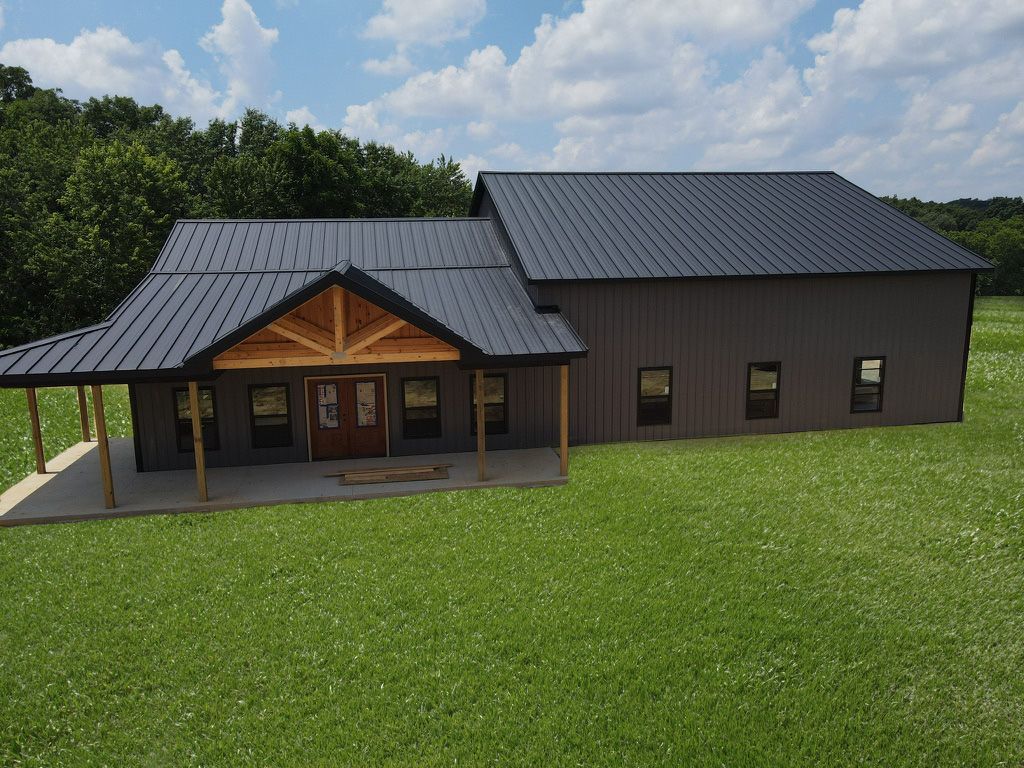 Modern dark-gray house with a covered porch on a grassy lawn, backed by trees.