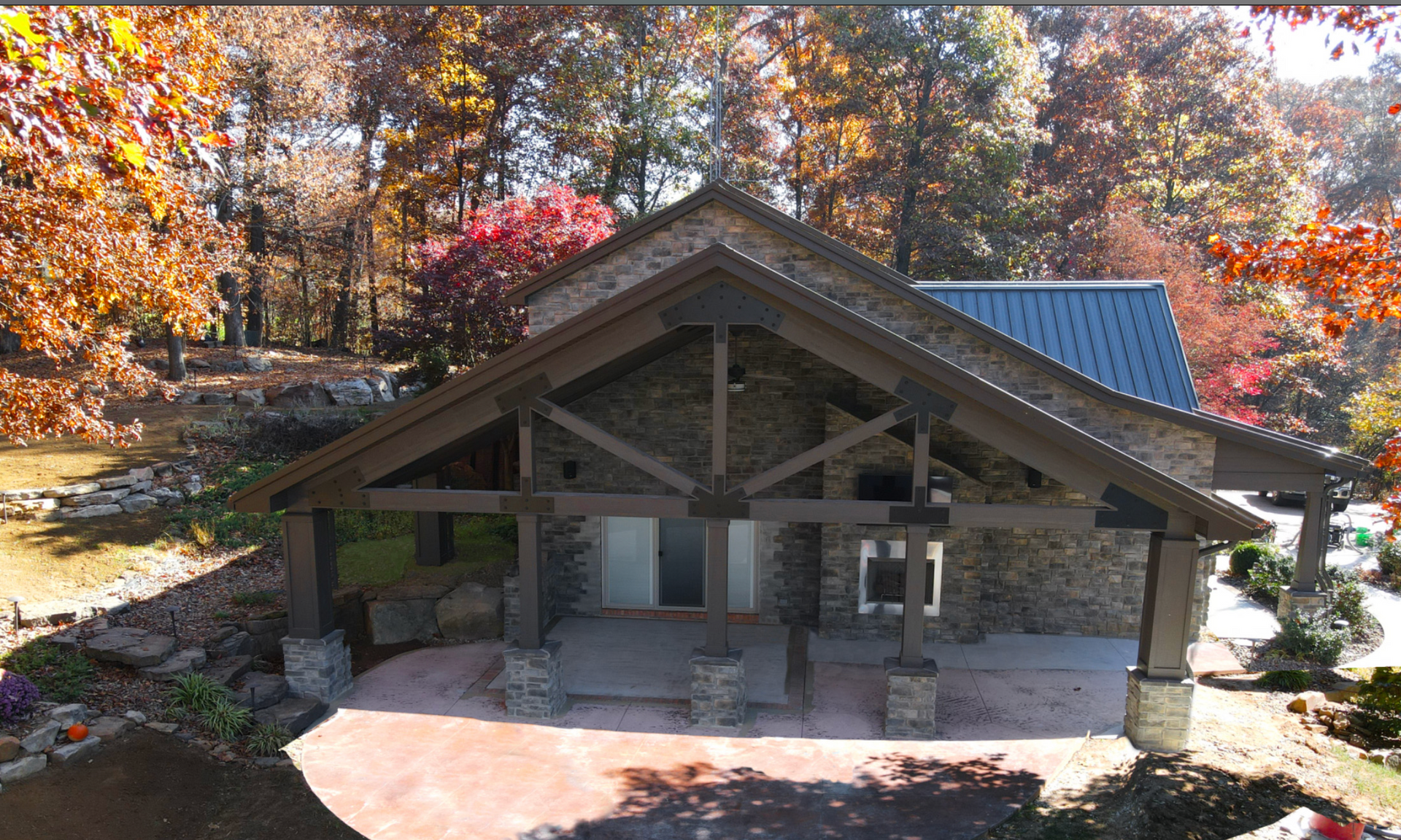 Stone cabin with a covered porch in autumn woods, surrounded by colorful fall foliage.